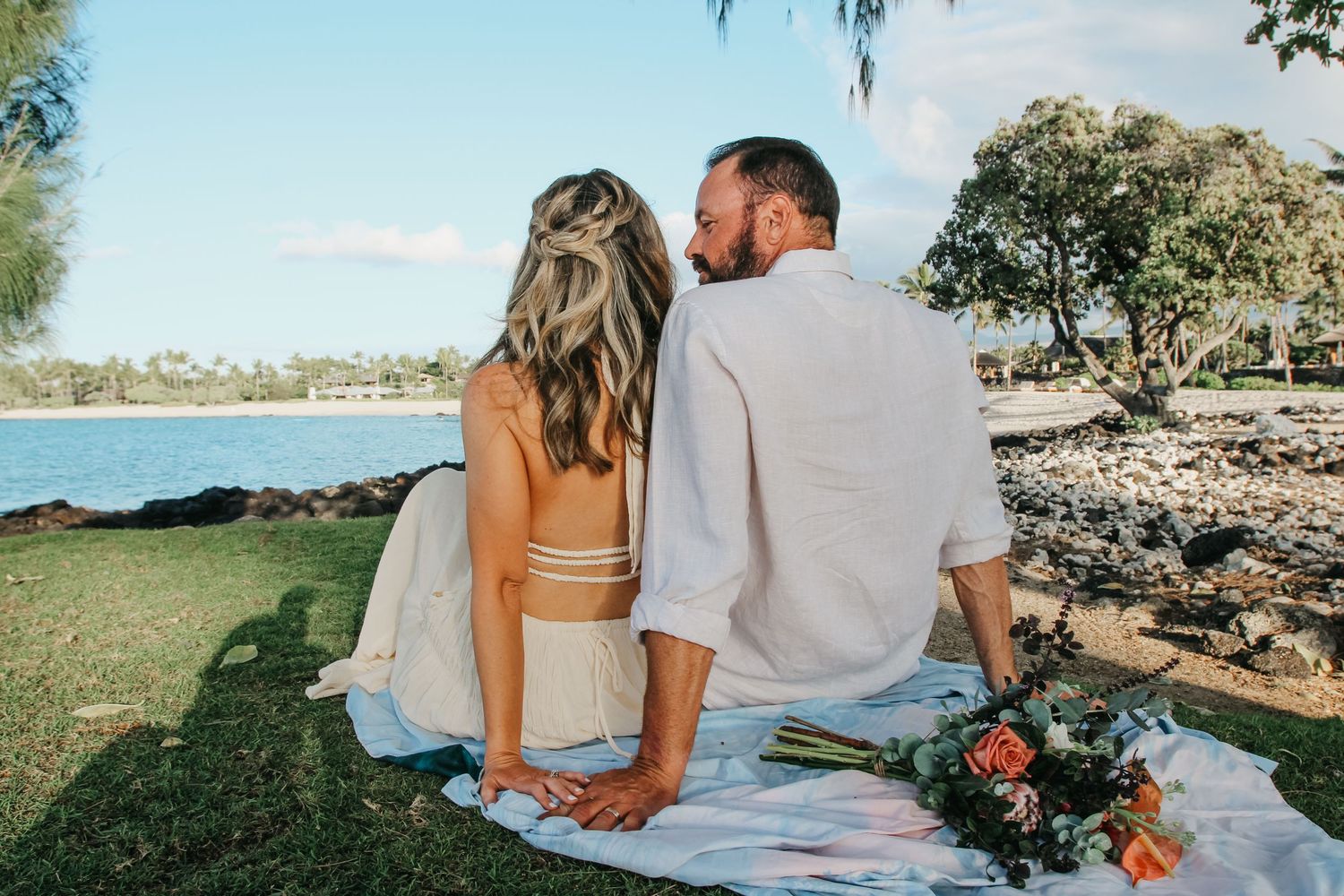 Couple sitting on grass with backs to camera looking at ocean at sunset at Kaikaua Point Beach Park Kona Hawaii