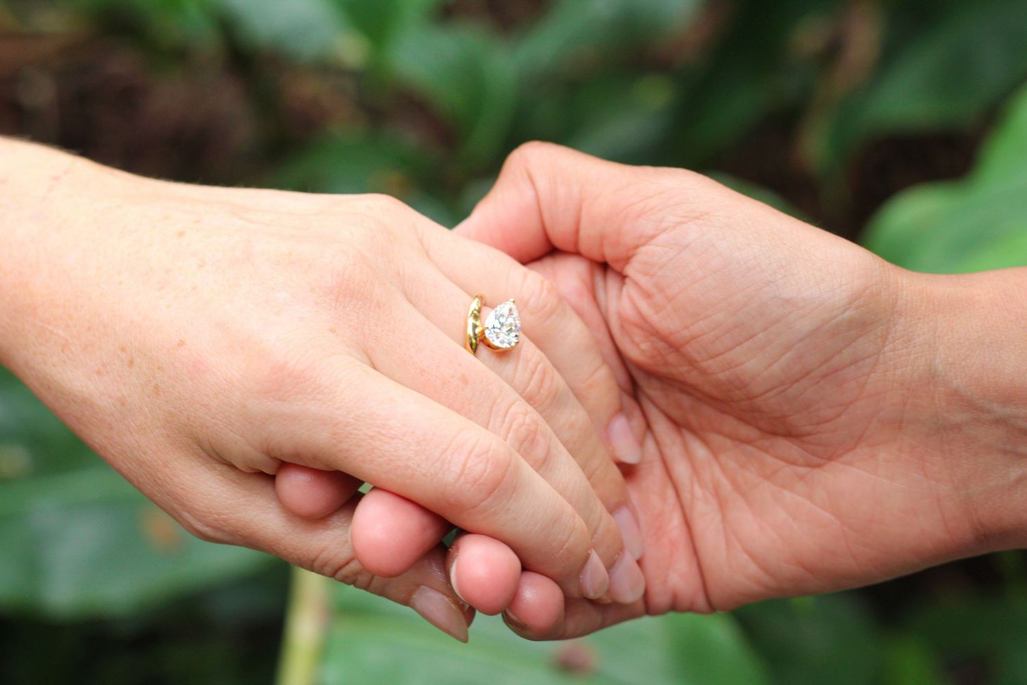 Close-up of wedding rings and hands during marriage ceremony in Kaloko rainforest Hawaii with jungle backdrop