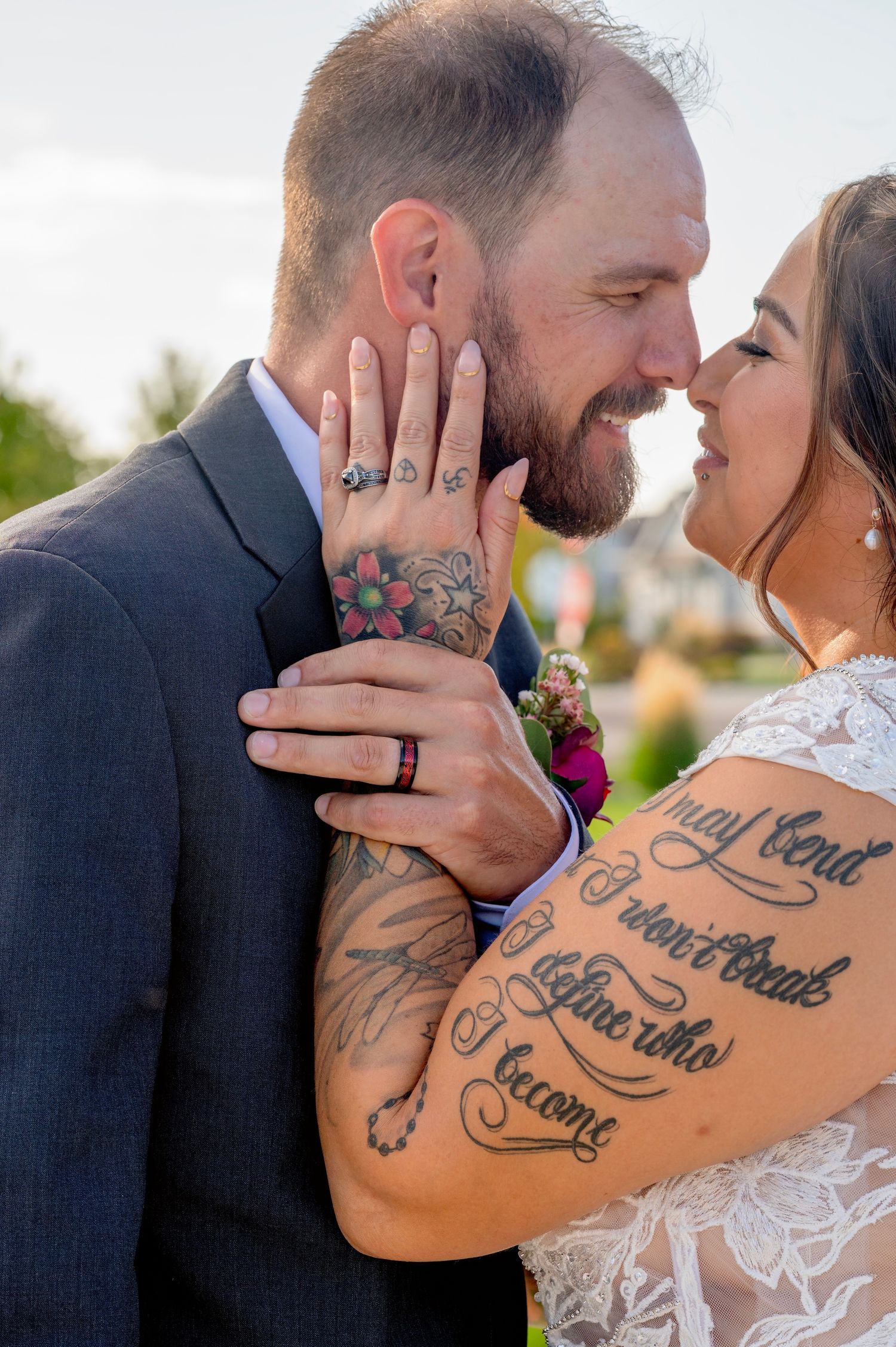Bride and groom with tattoos touching foreheads and smiling during outdoor wedding portrait session.