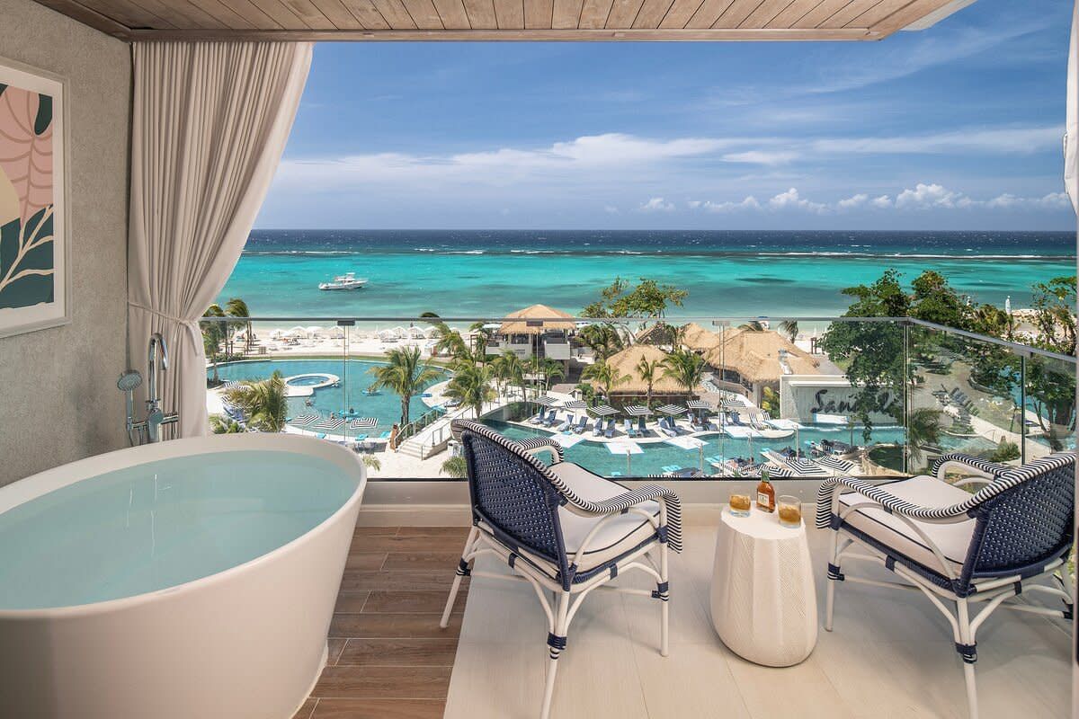 Luxurious overwater villa balcony with freestanding soaking tub overlooking turquoise Caribbean ocean and resort pool.