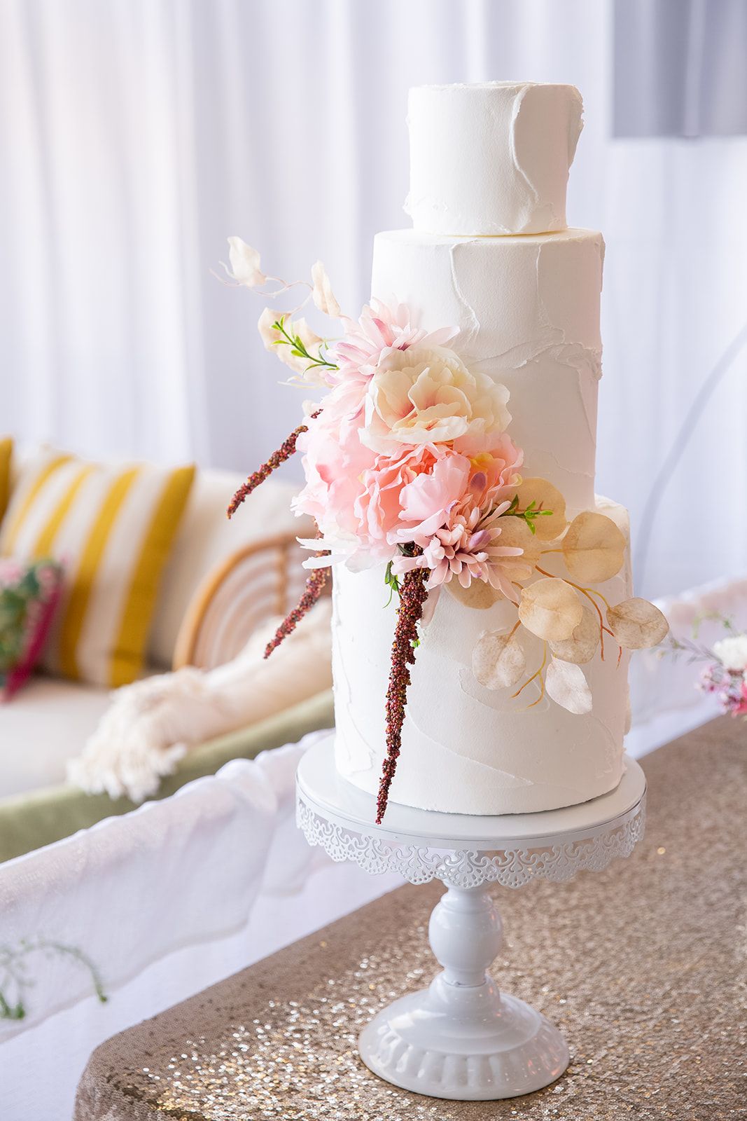 A three-tier white wedding cake adorned with pink and cream floral decorations on a stand.