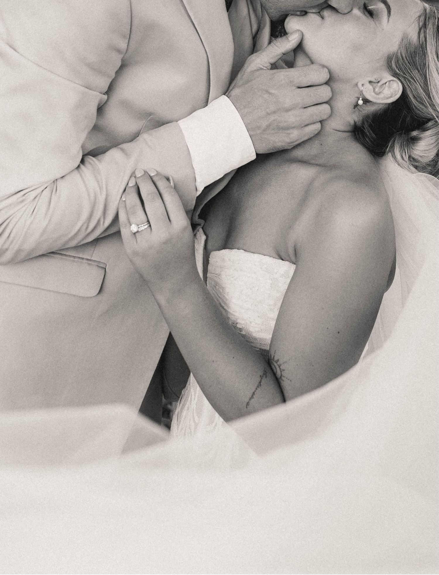 Black and white wedding photo of bride and groom sharing a romantic kiss, bride wearing strapless gown and diamond ring.