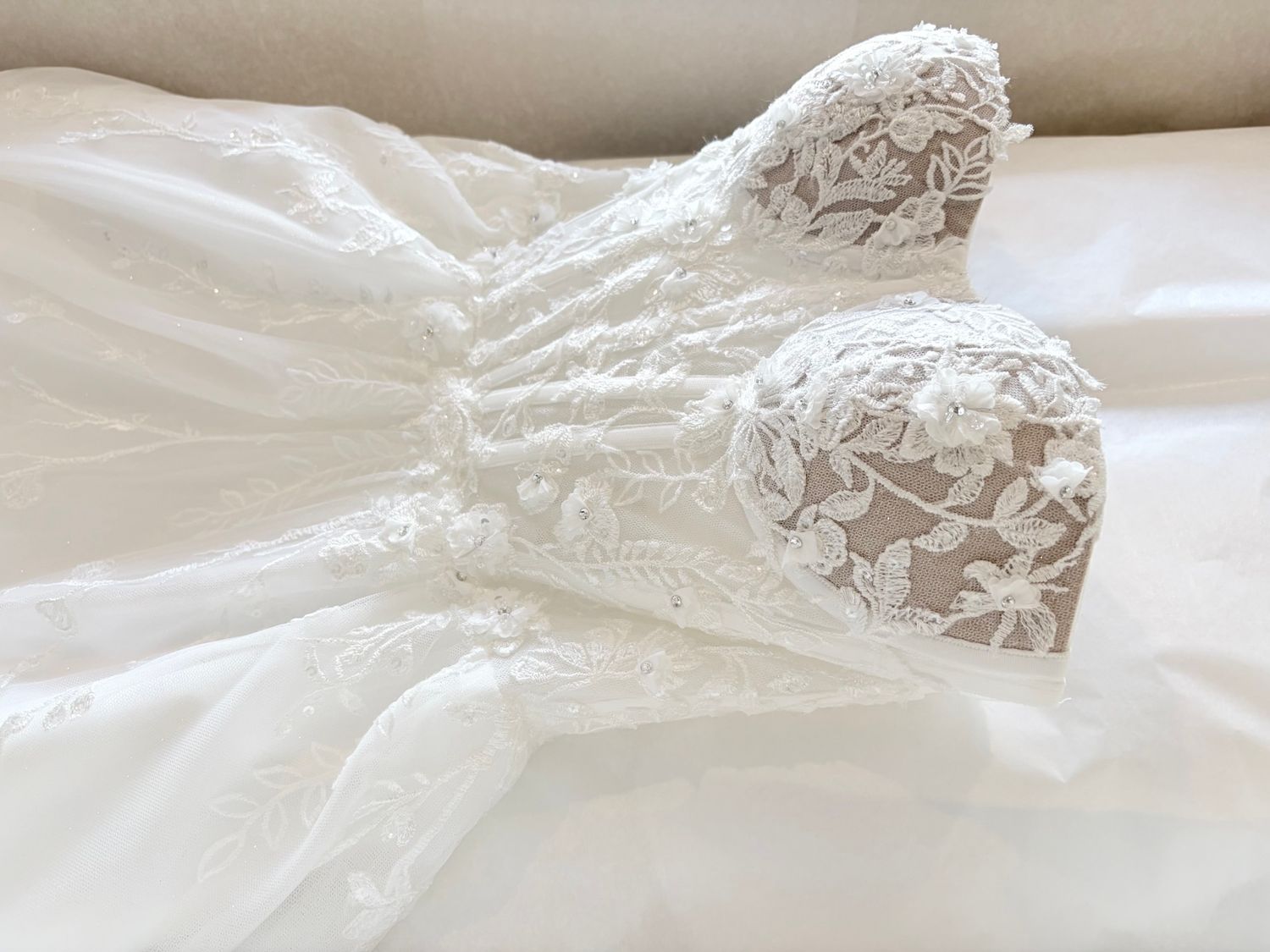 White lace wedding dress with floral embroidery and sheer bodice laid flat on white surface.