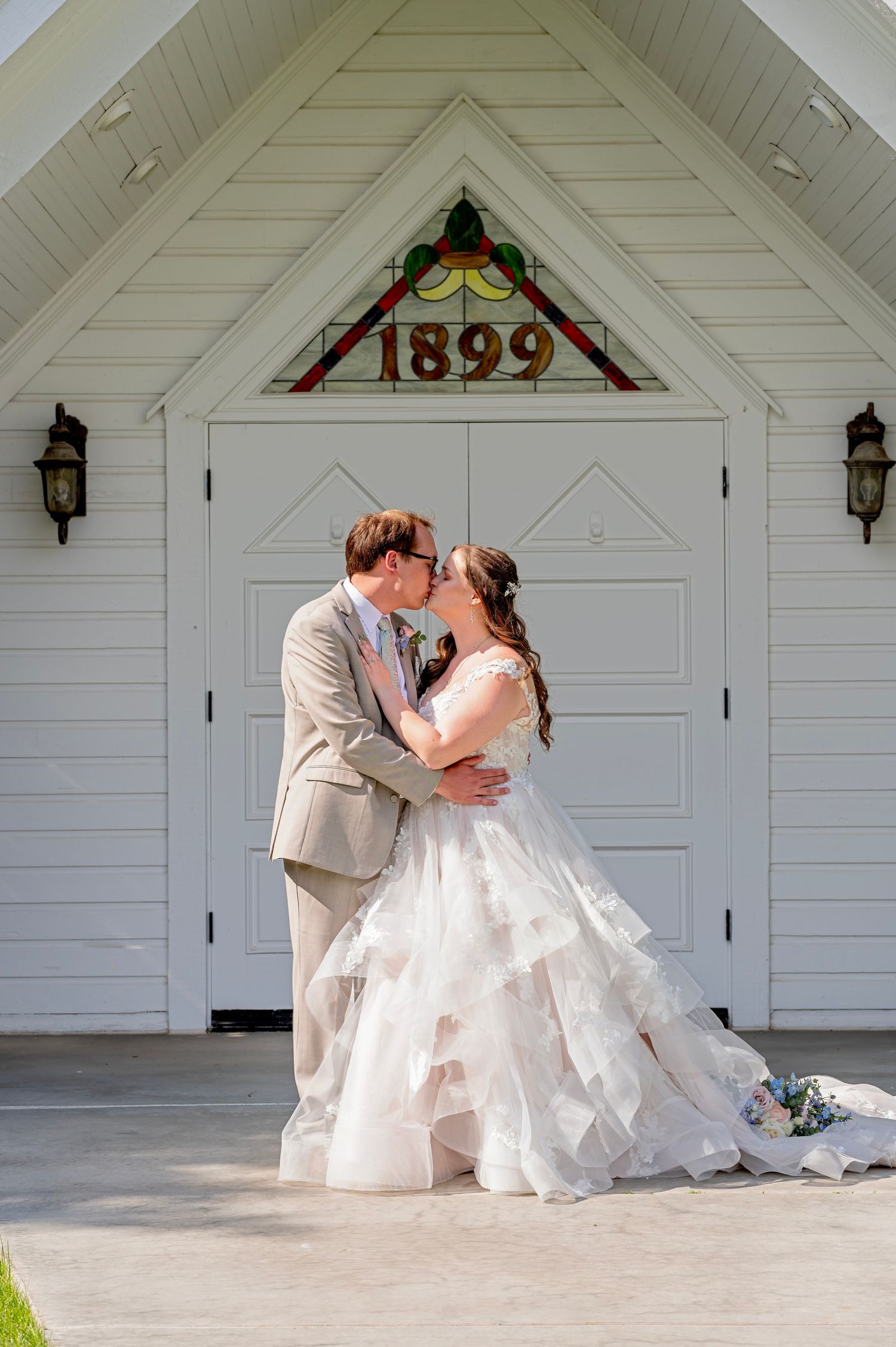 Bride and groom share a first kiss outside a historic white chapel built in 1899 on their wedding day.
