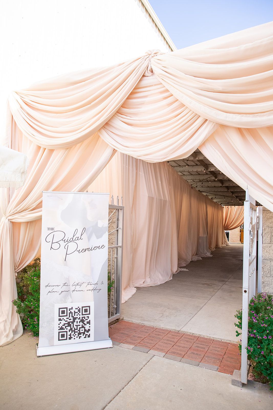 A blush fabric-draped pergola entrance with a Bridal Premiere banner and QR code display.