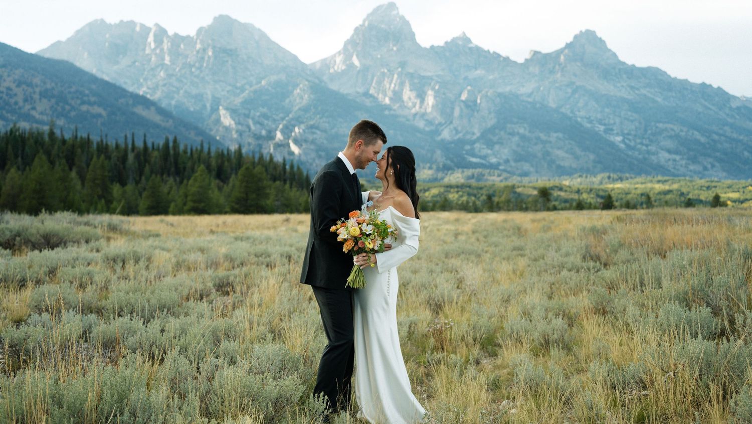 Bride and groom sharing romantic moment in field with Grand Teton mountains backdrop.