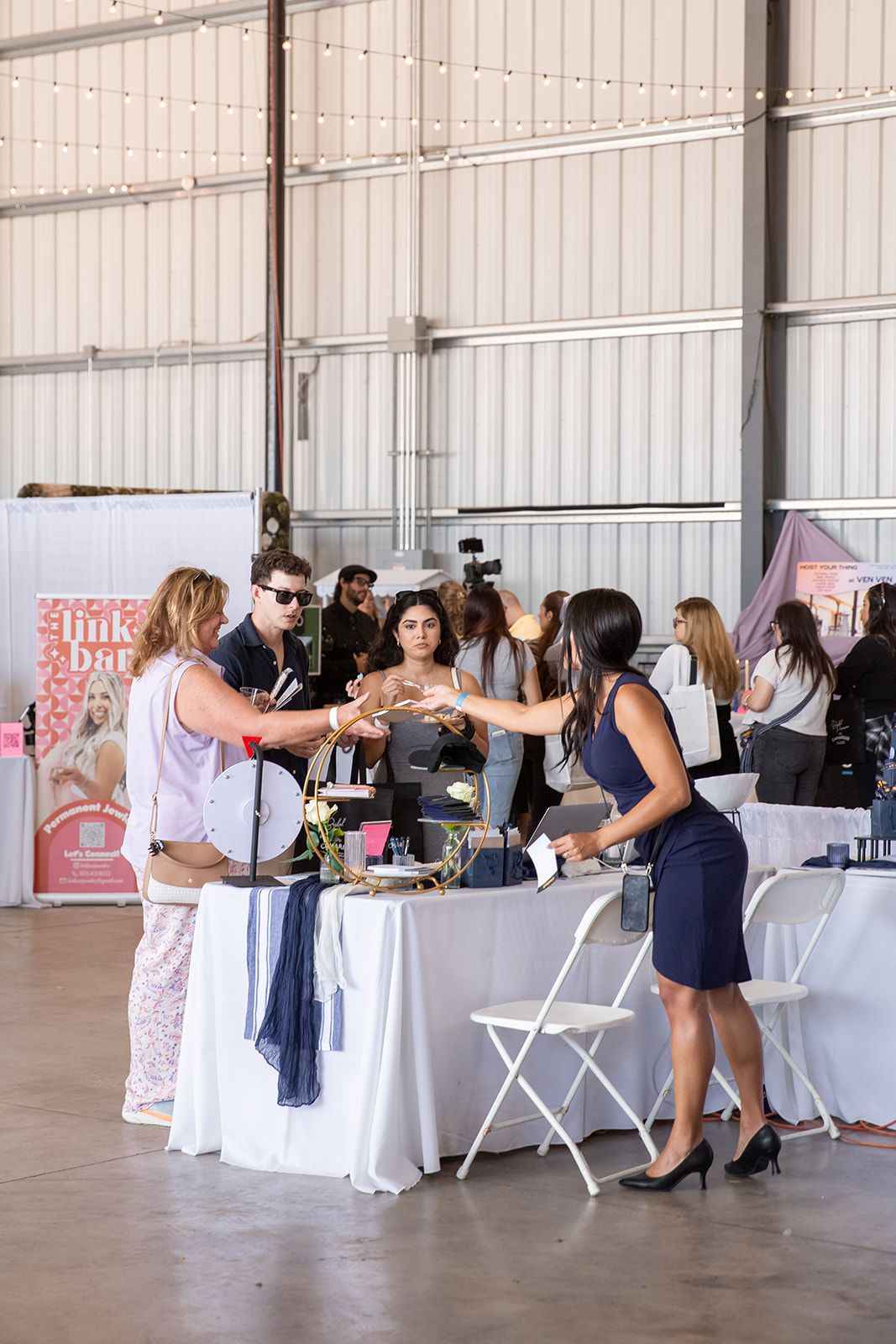 Guests interact with vendors at a bridal expo inside a large industrial hangar venue.