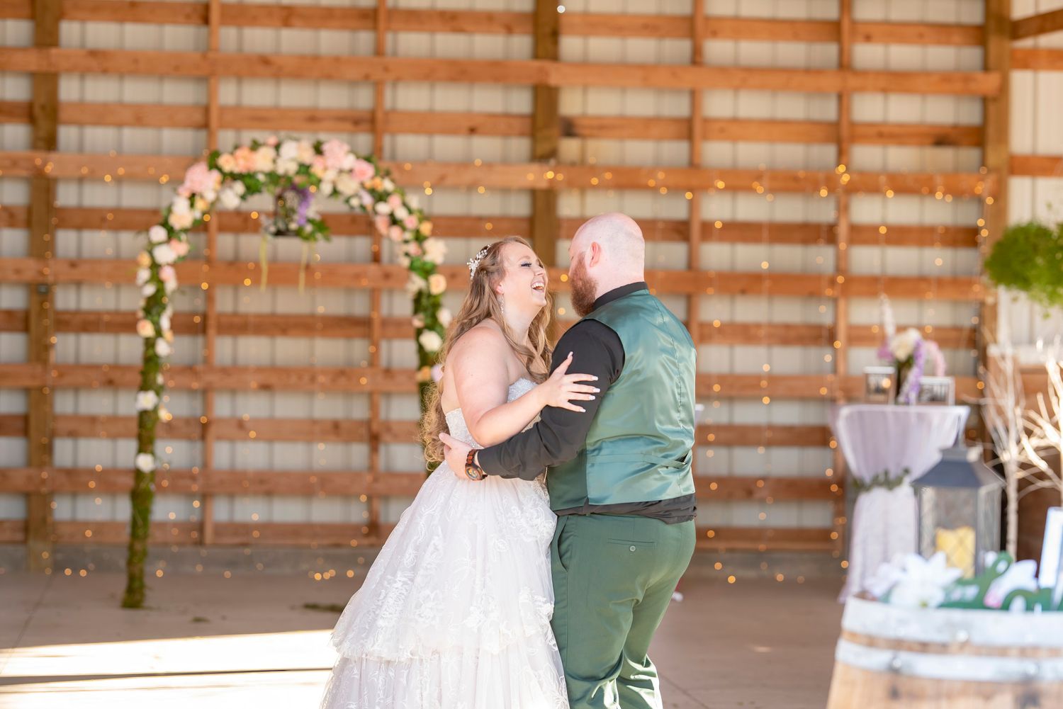 Bride and groom sharing their first dance under a floral arch in a rustic barn wedding venue.
