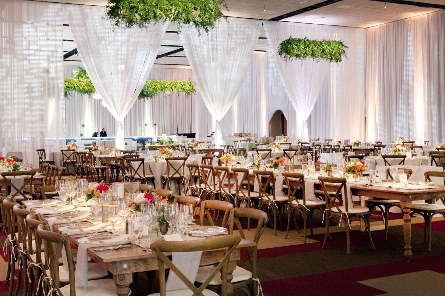 Elegant wedding reception hall with greenery installations and rustic wood chairs.