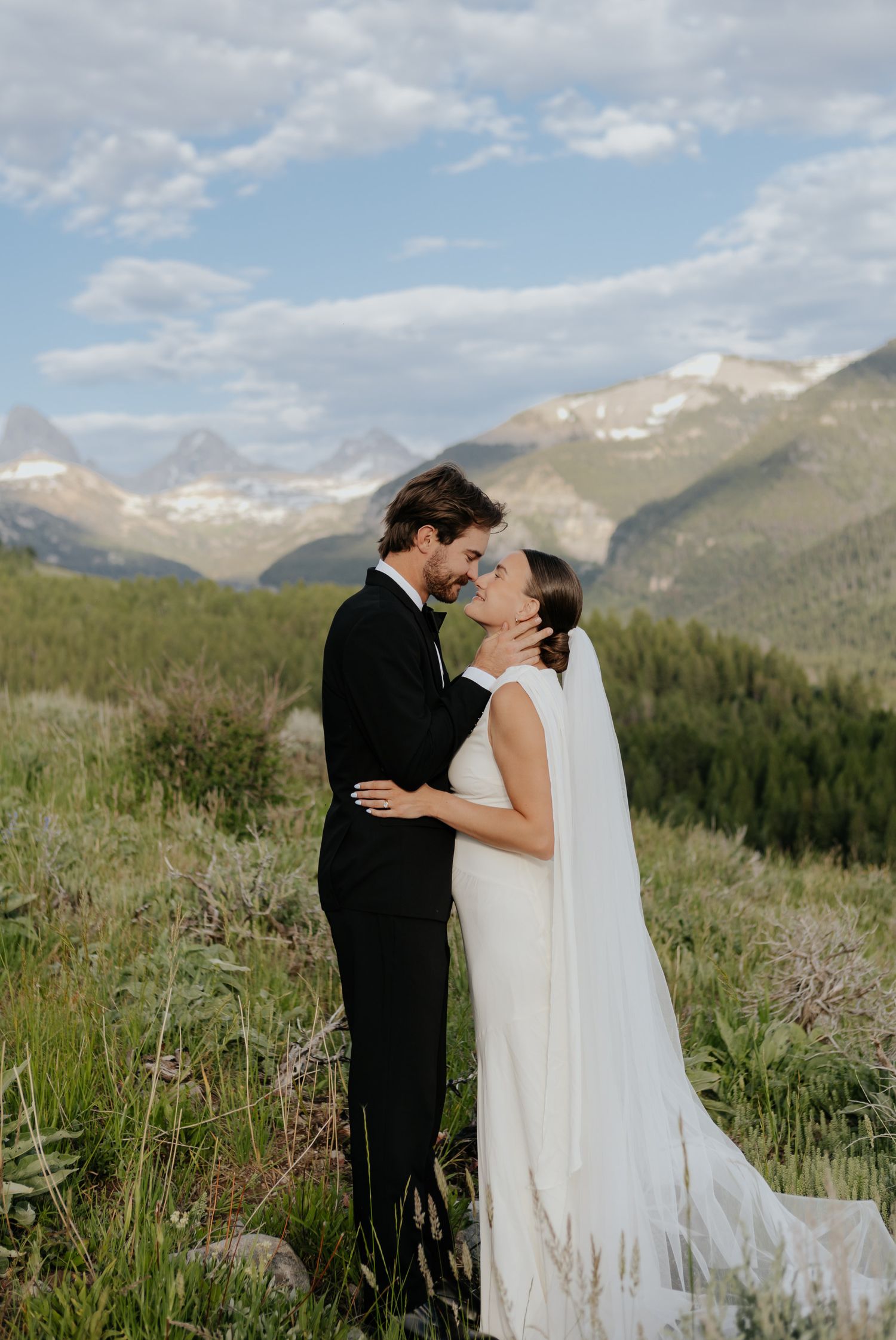 Bride and groom share a romantic moment with stunning mountain views and lush greenery in the background.
