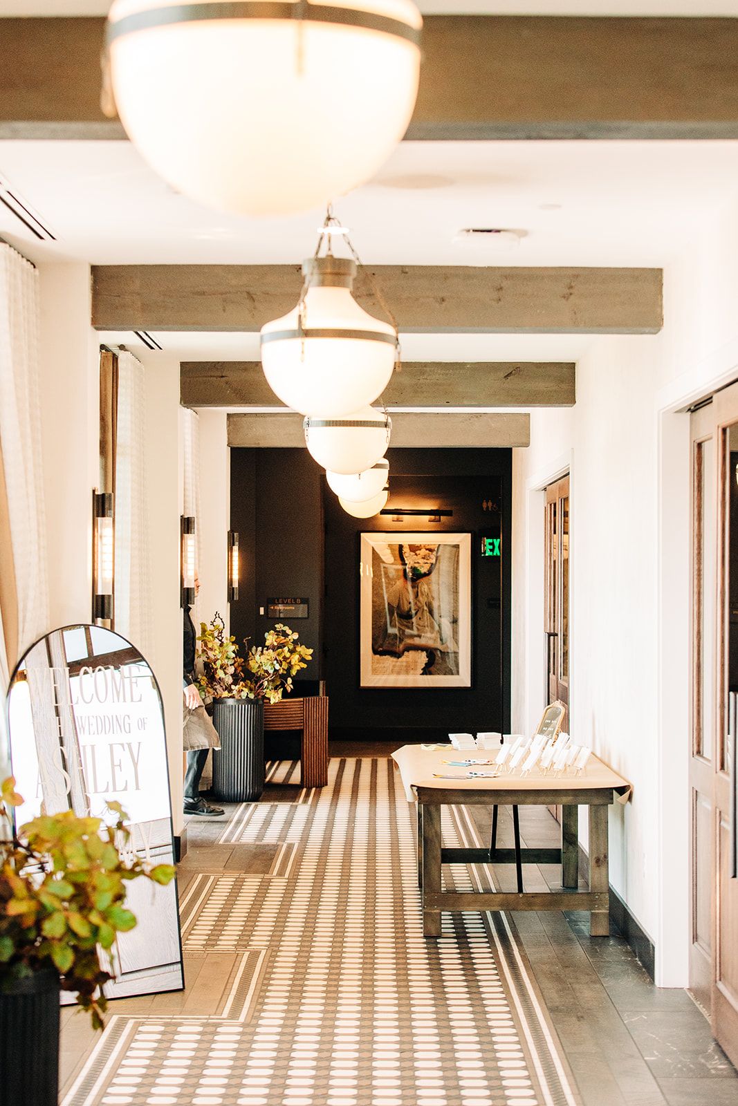Bright hotel corridor with patterned tile floor, pendant lights, and welcome wedding signage.