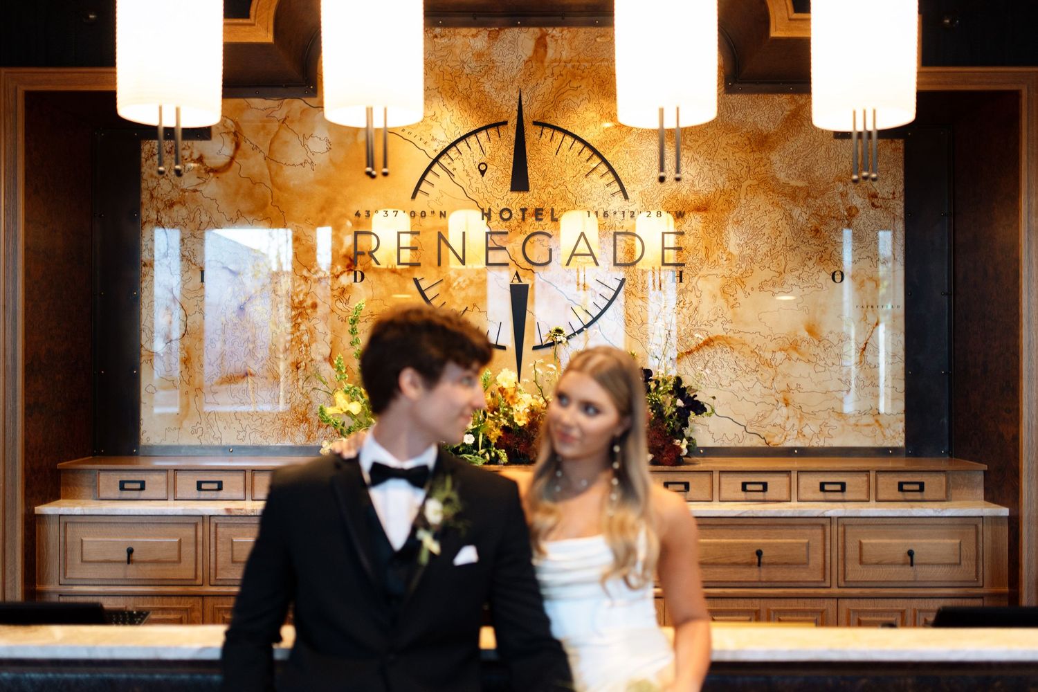 Bride and groom pose before Hotel Renegade lobby sign with golden marble wall backdrop.