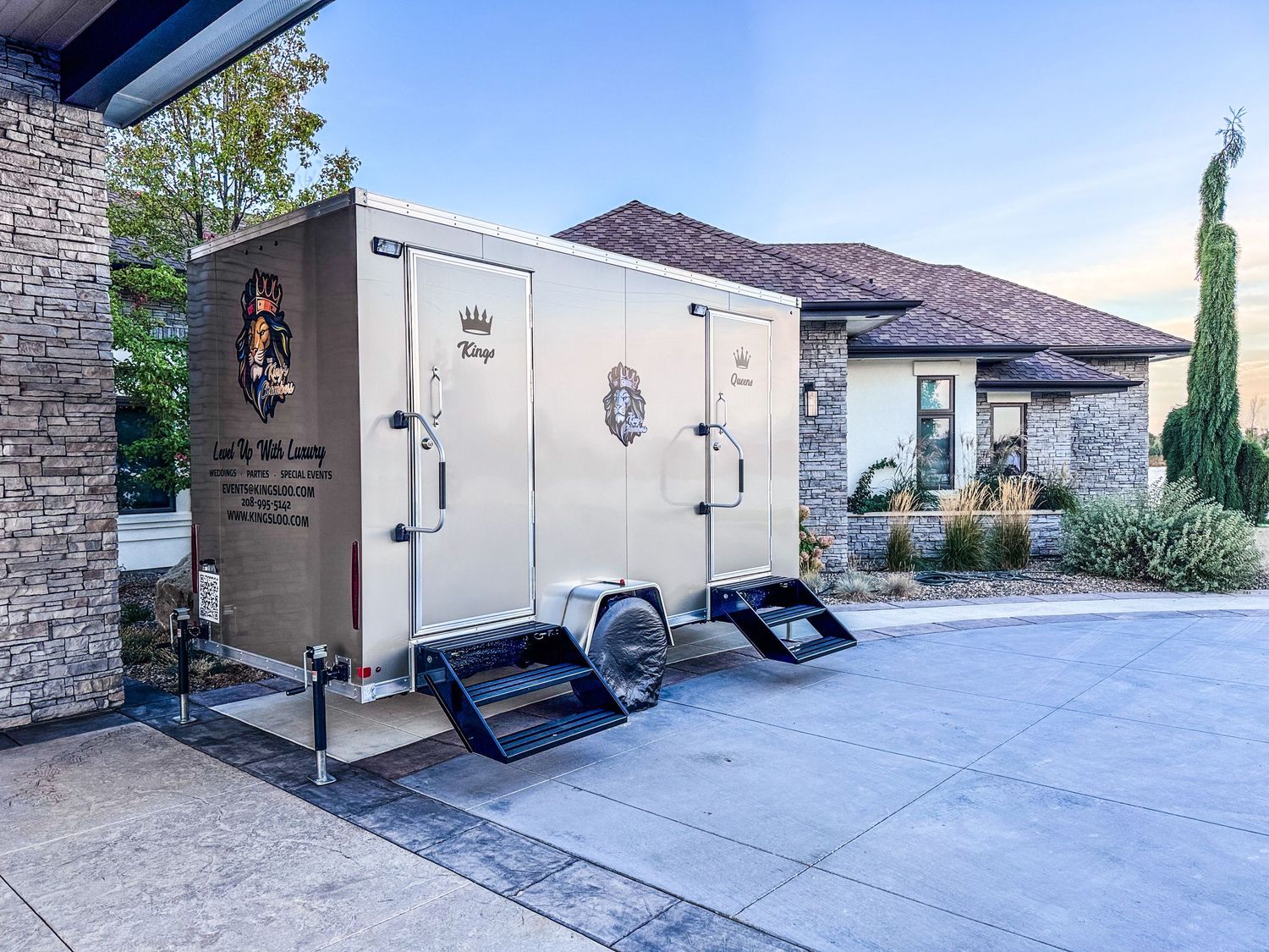 Luxury portable restroom trailer with ramps parked in a driveway outside an upscale home.
