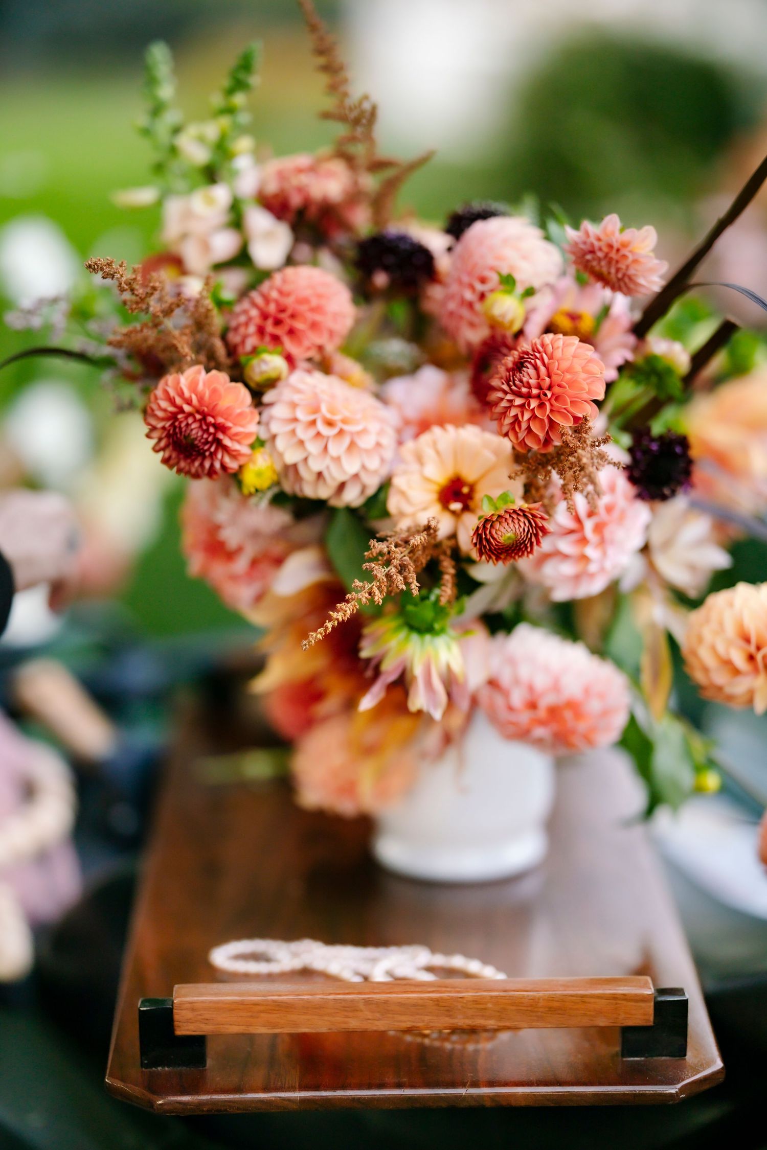 Lush peach and coral dahlia floral arrangement in a white vase on a wooden tray.