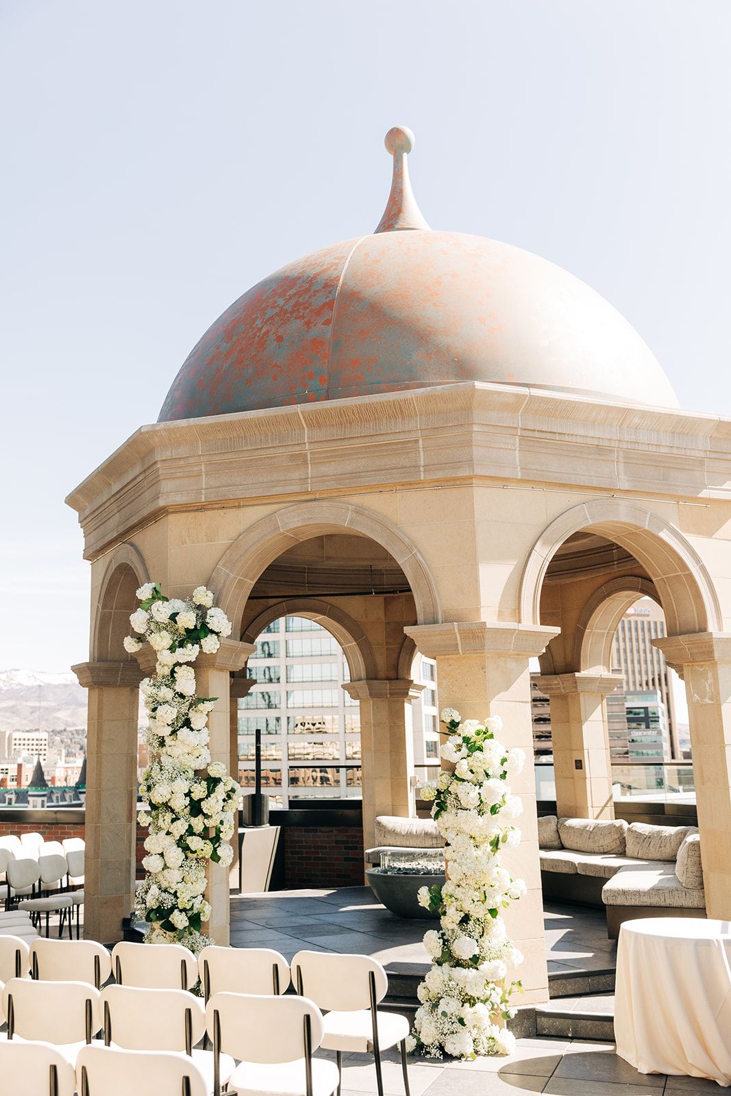 Rooftop wedding ceremony setup with white floral arrangements beneath ornate copper dome.