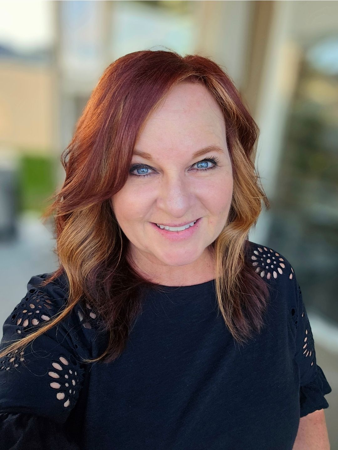 Smiling woman with auburn hair and blue eyes wearing black top in professional headshot photo.