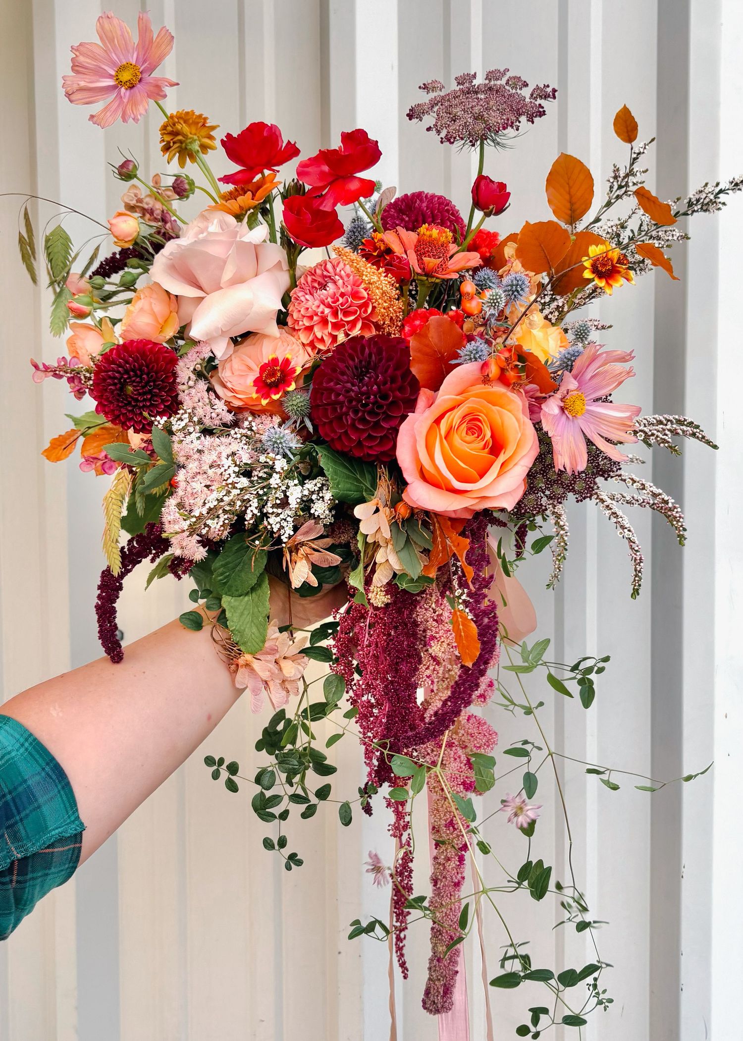 Vibrant cascading bridal bouquet with red, orange, and pink seasonal blooms.