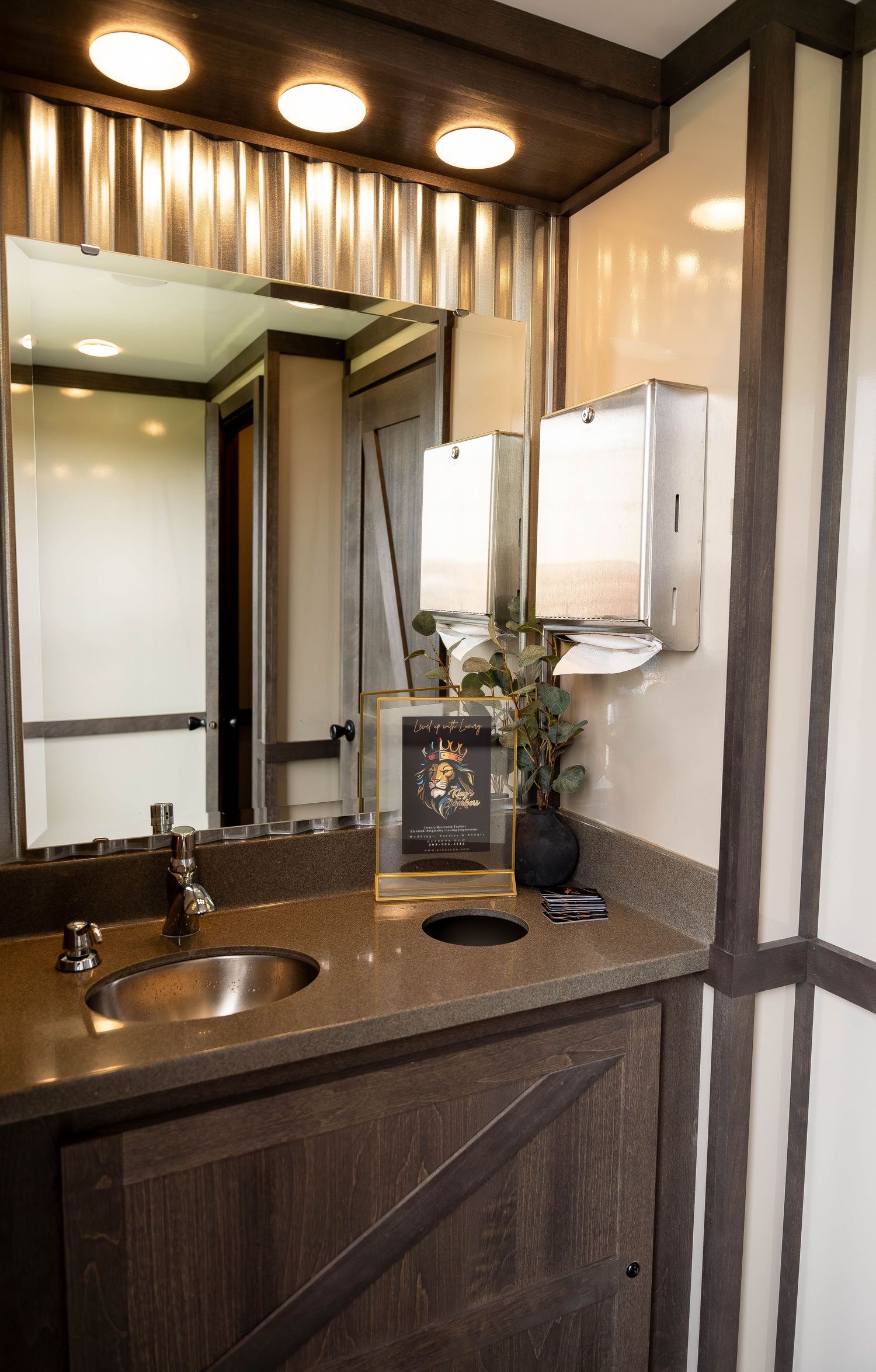 Elegant portable restroom interior with copper sink, granite countertop, large mirror, and modern dispensers.
