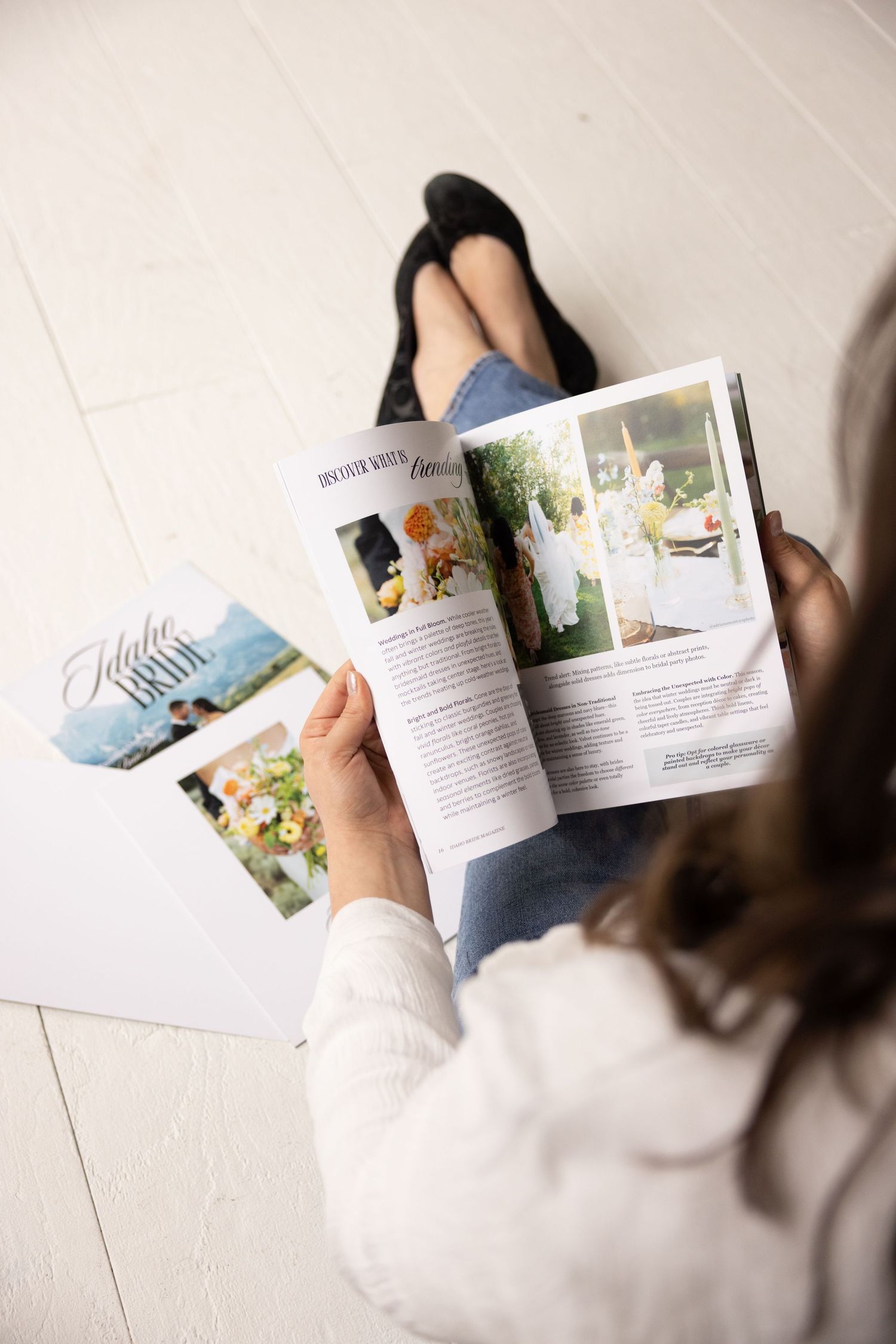 Woman sitting on white floor reading Idaho Bride magazine with bouquet photo visible.