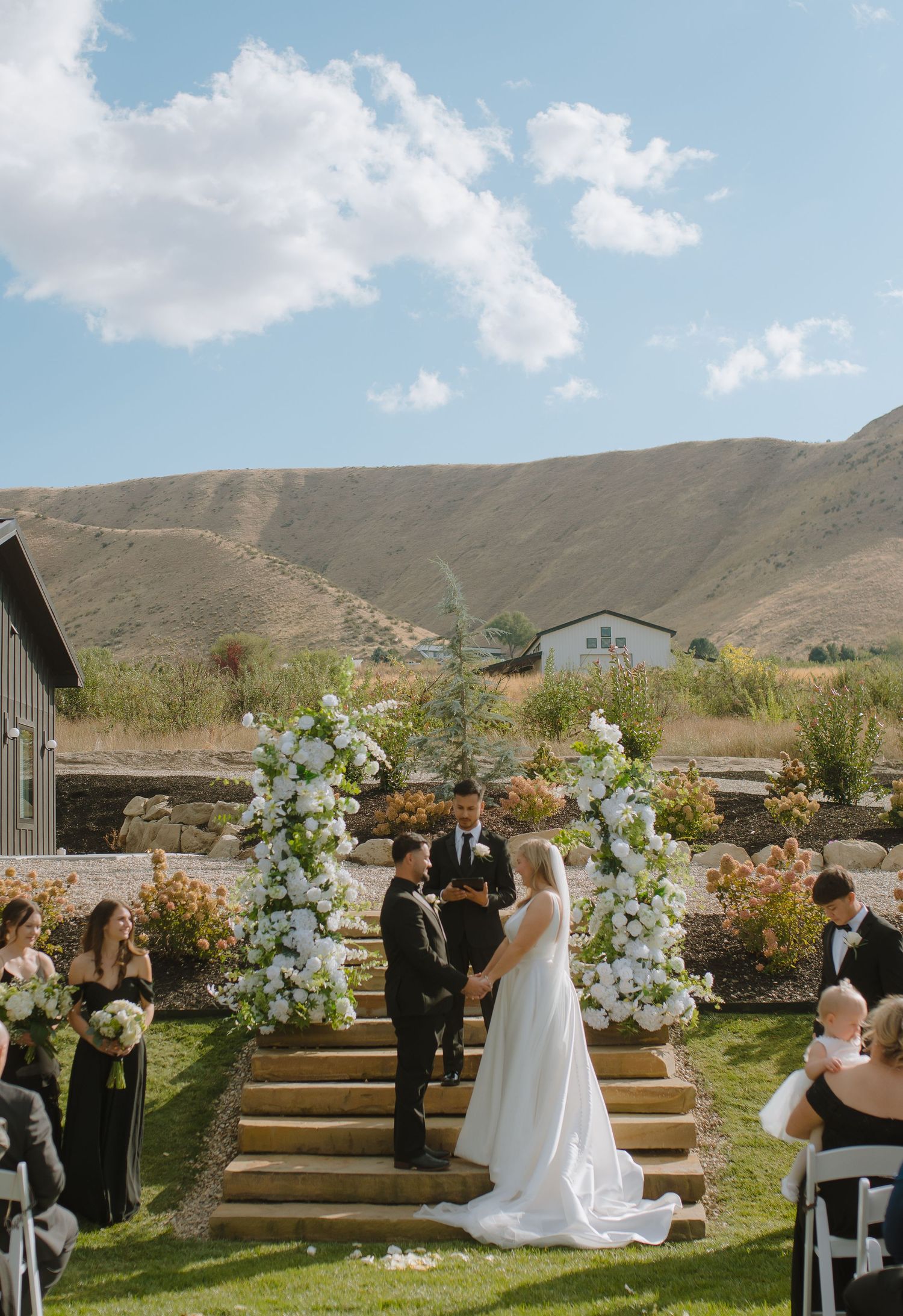 Outdoor wedding ceremony with white floral arch and mountain backdrop.