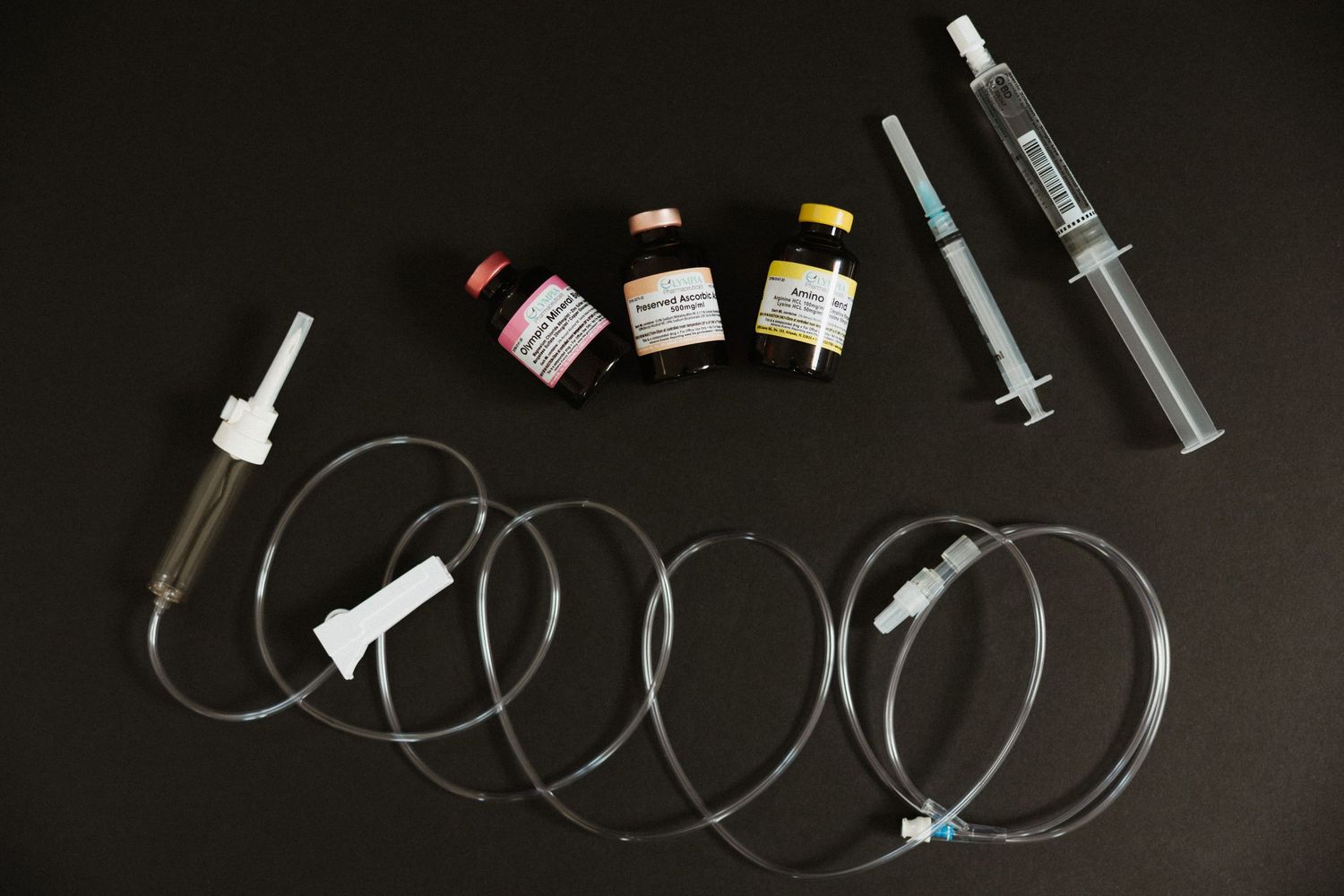 Medical syringes, IV tubing, and small medication vials arranged on a dark background.