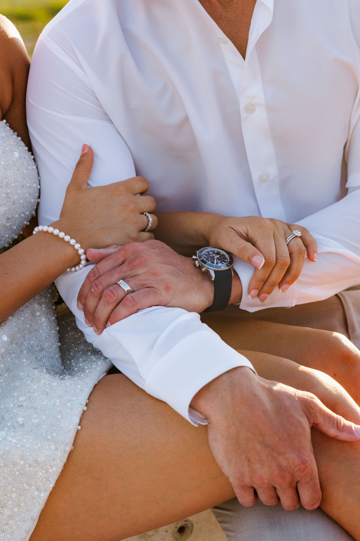 Close-up of bride and groom hands showing wedding rings, pearl bracelet, and luxury watch.