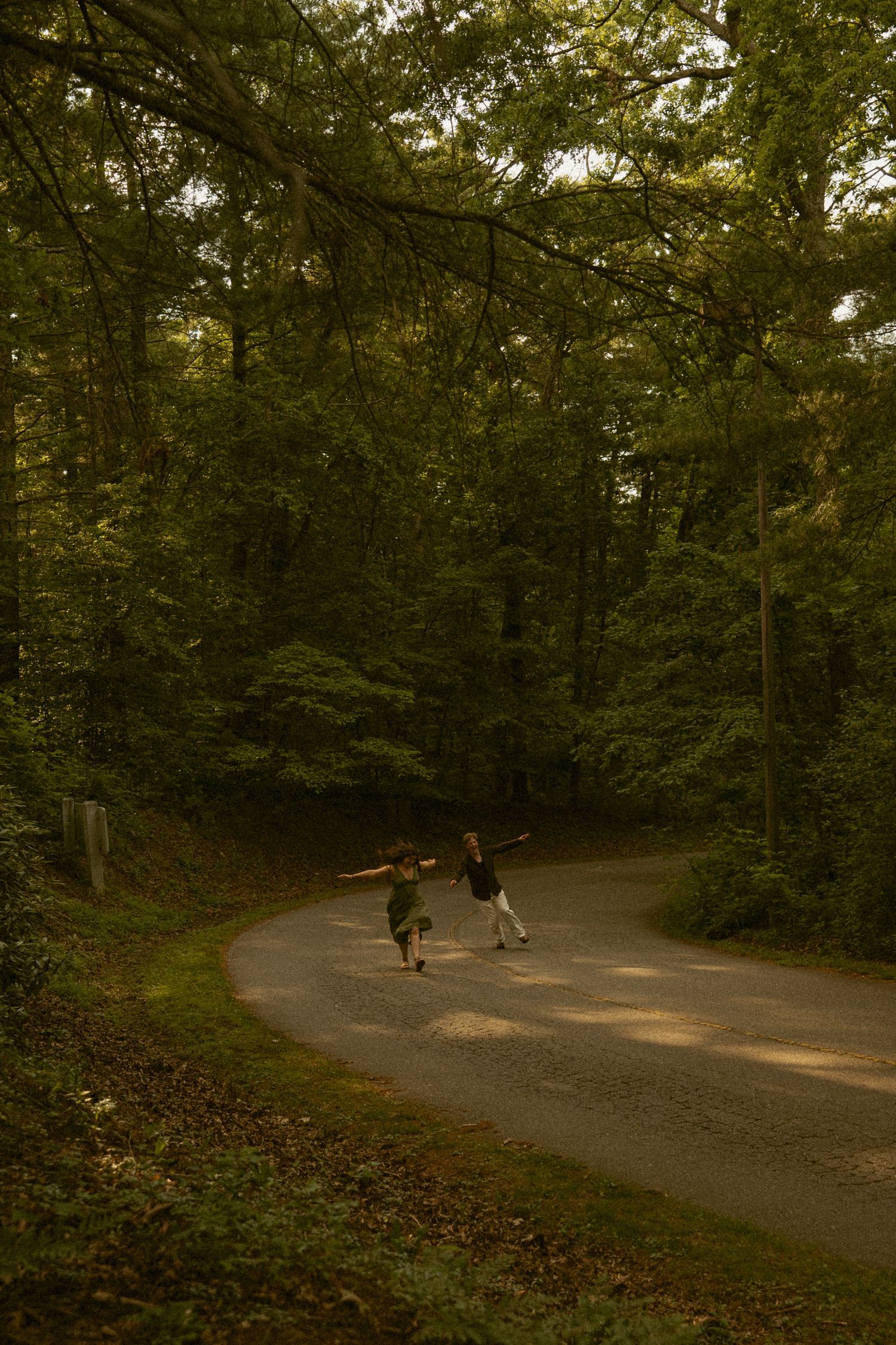 Two children running along a winding forest road surrounded by lush green trees in a serene woodland setting.