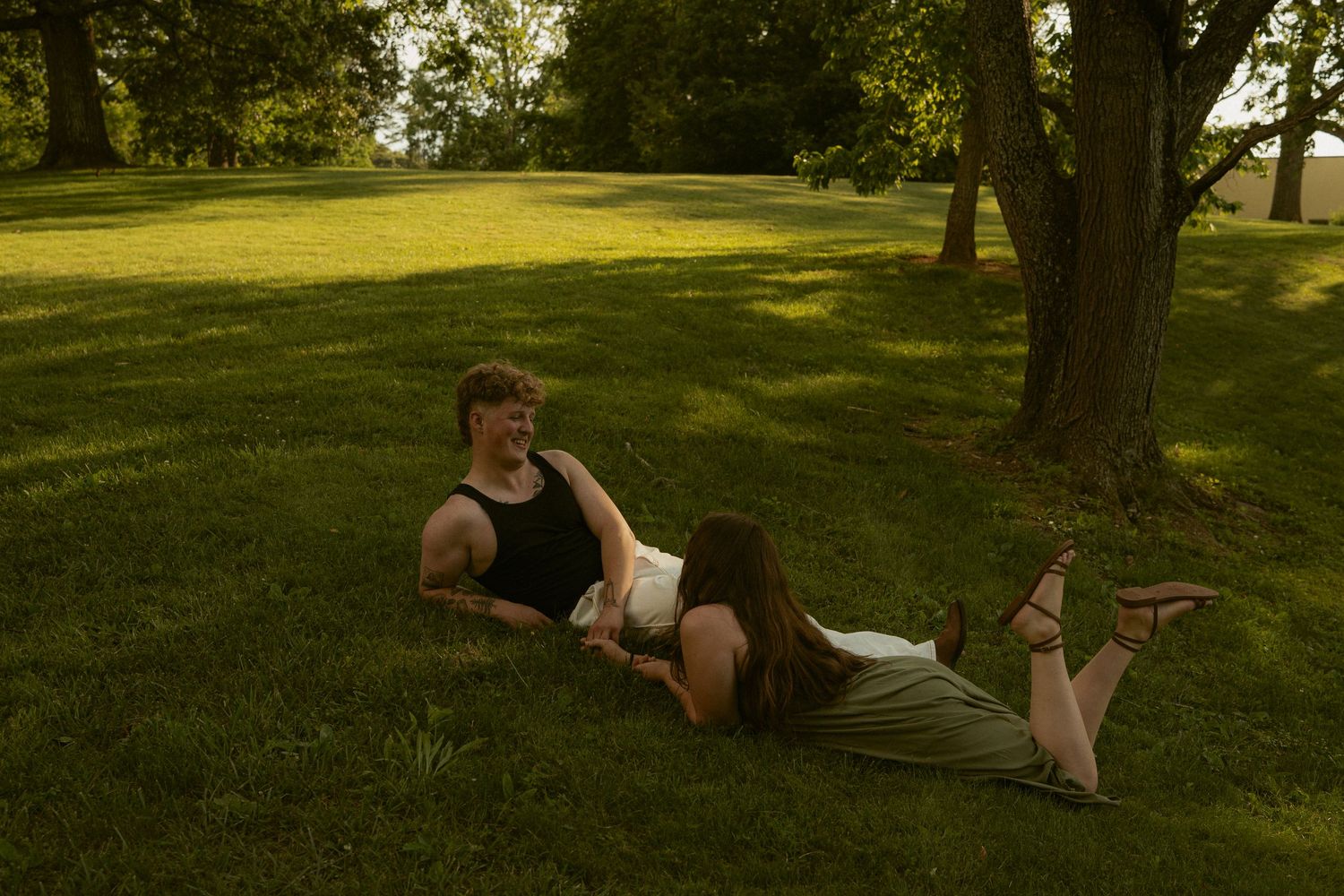 Couple relaxing on green grass in a park, man sitting while woman lies with head in his lap near a tree.