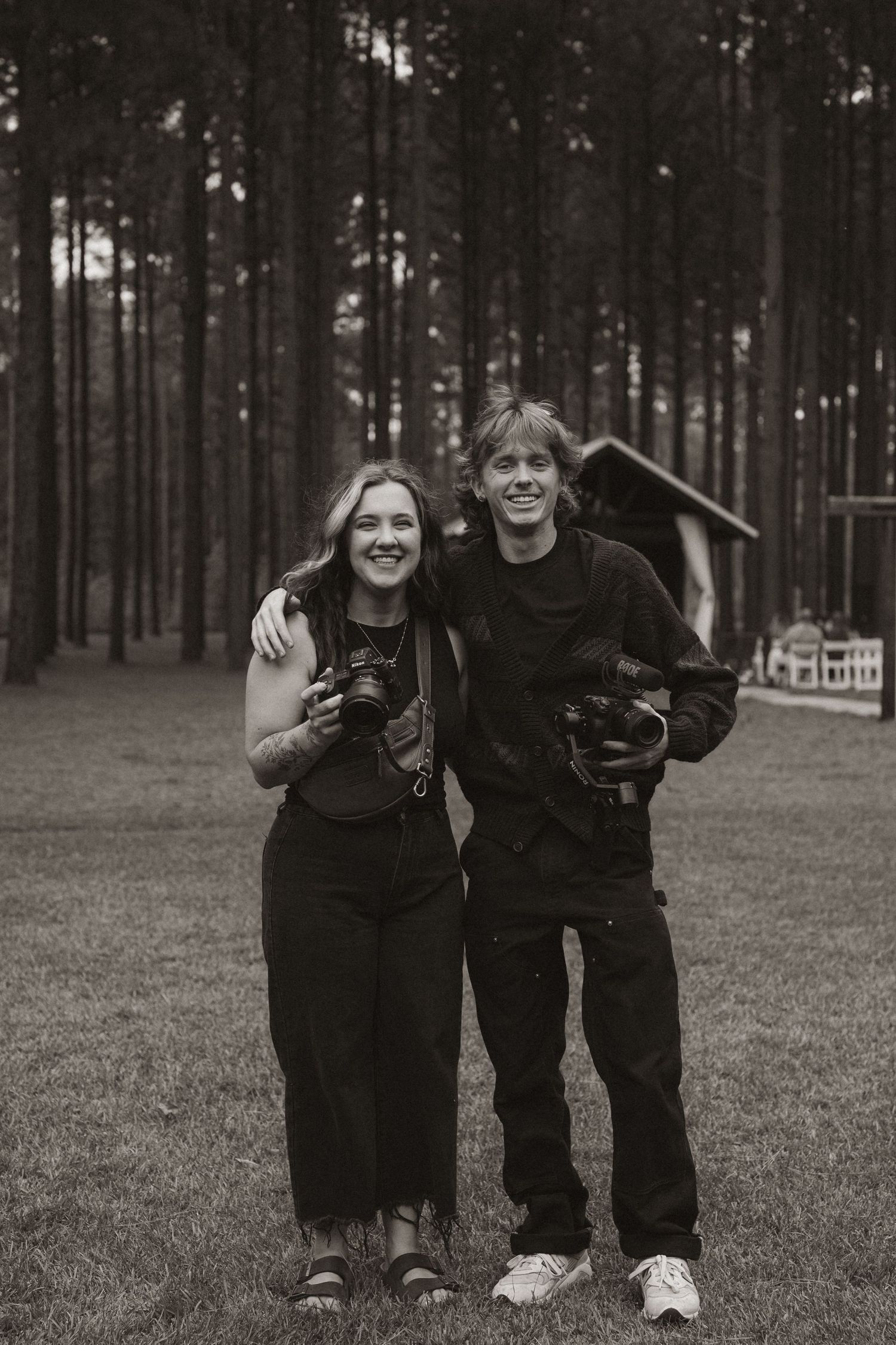 Two photographers standing together holding cameras in a forest setting.