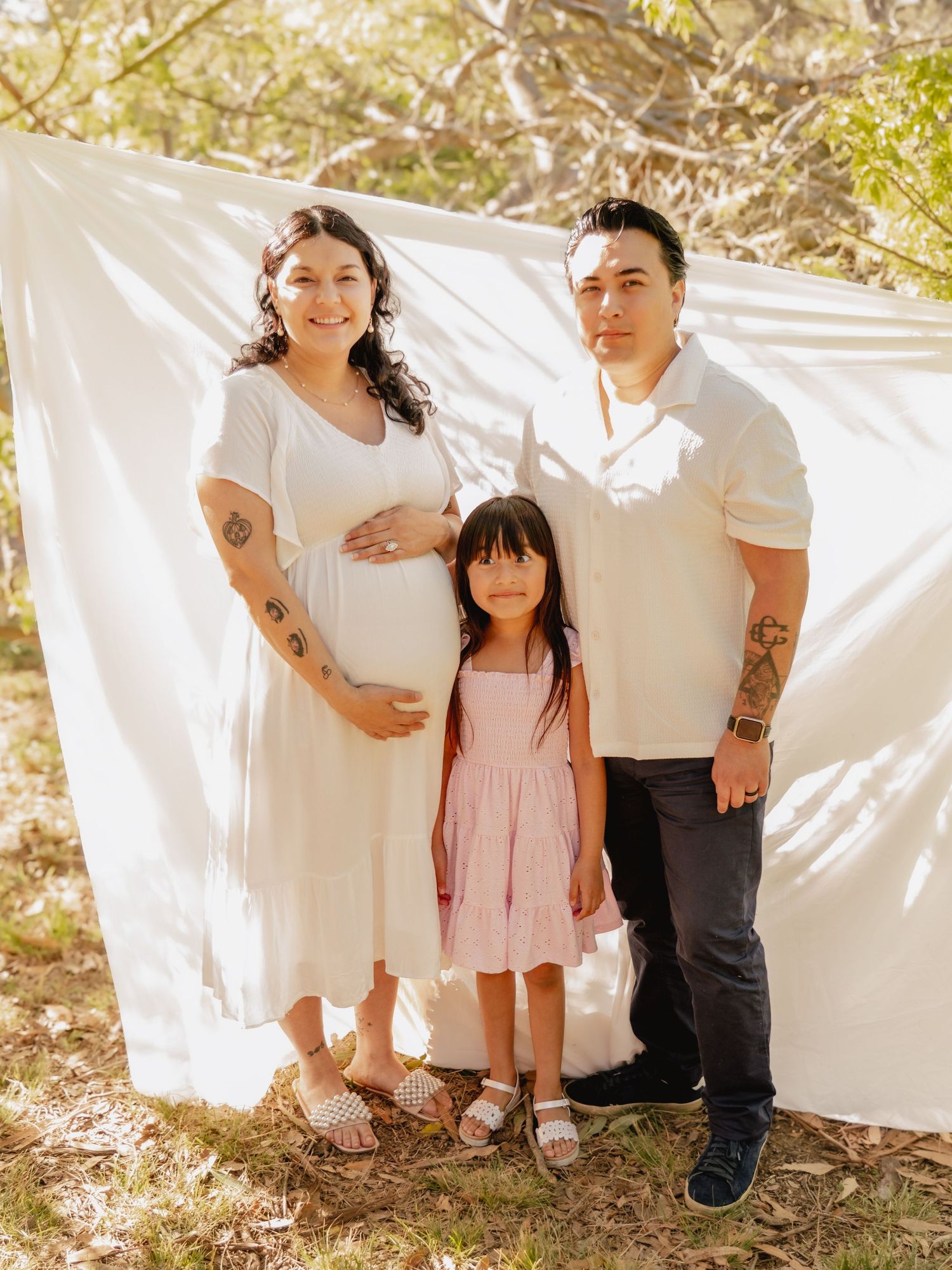 Family members peek out from behind white sheets hanging outdoors in a playful lifestyle photoshoot.