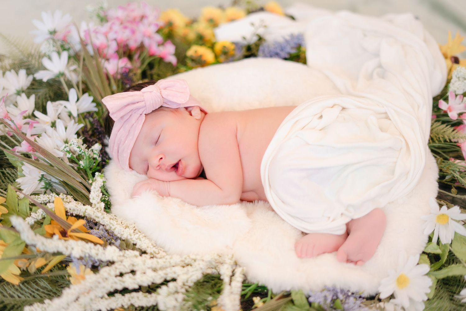 A newborn photography session featuring baby surrounded by yellow and white flowers.