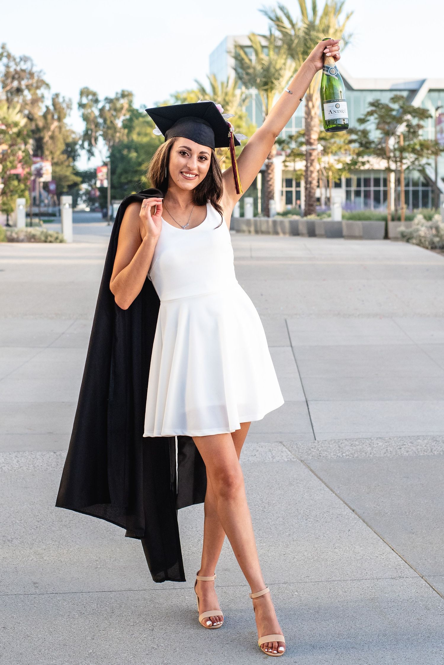 Graduate in white dress and cap twirls on campus plaza.