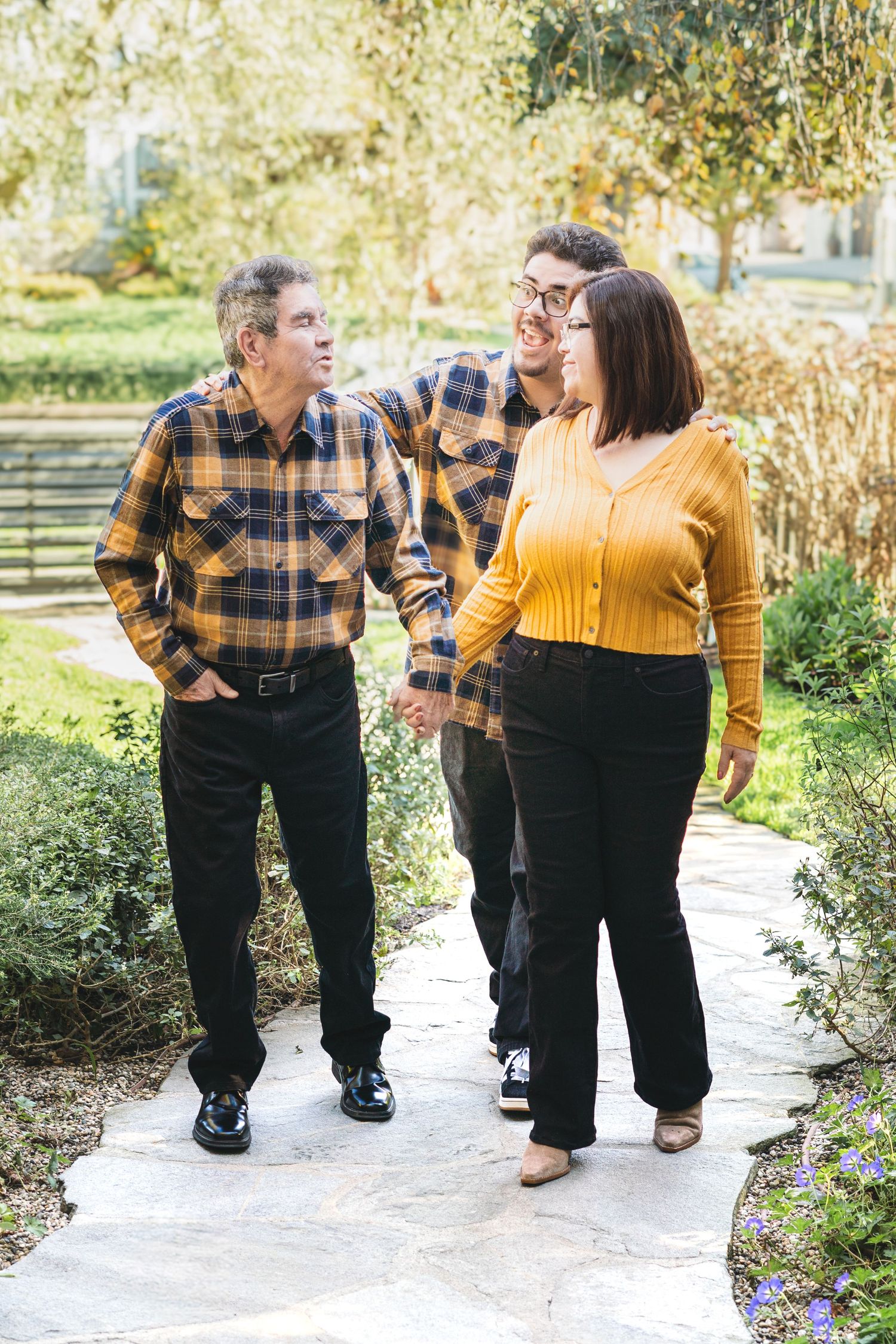 Family walking together on garden path wearing coordinated plaid and yellow sweaters on sunny autumn day.