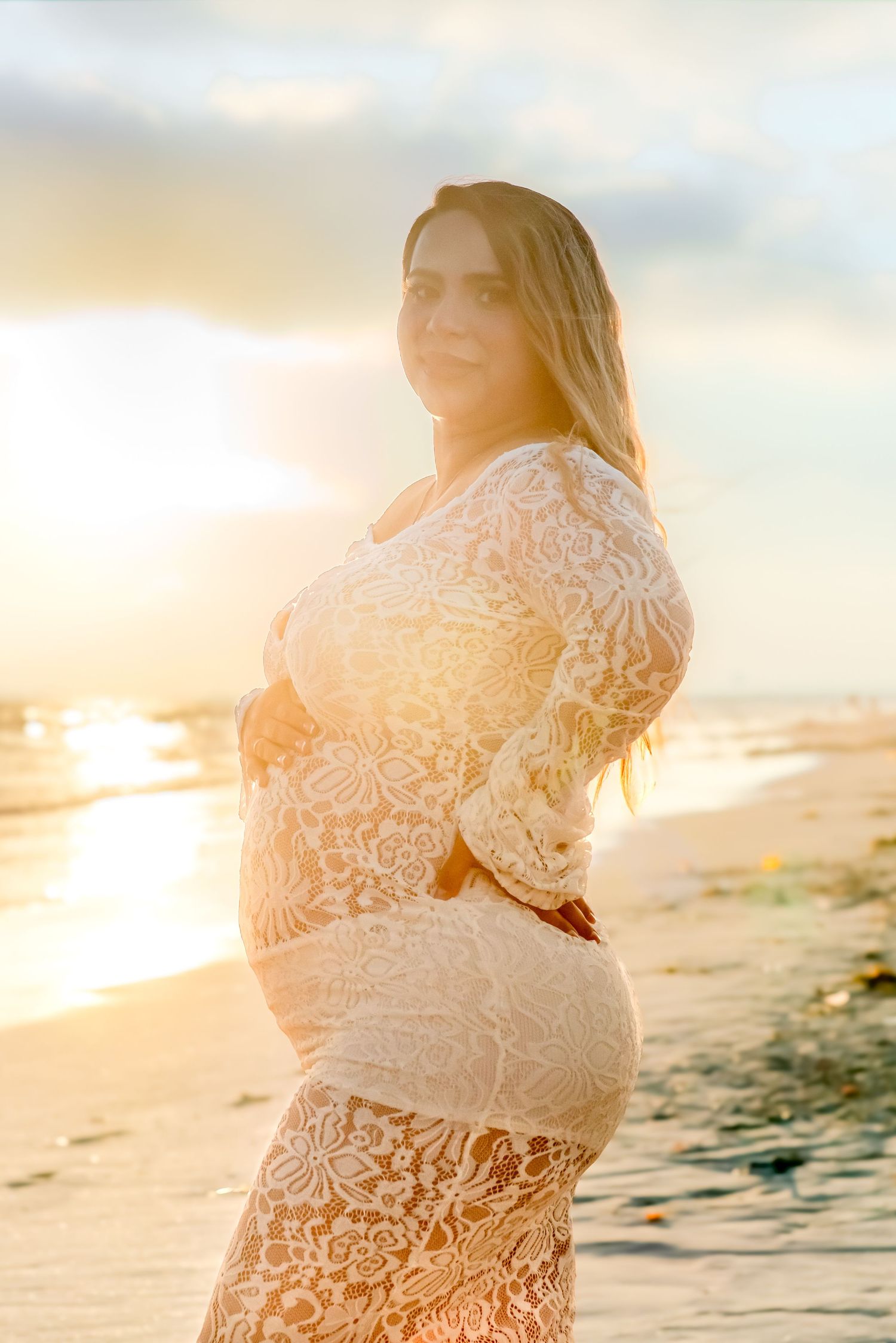 Maternity photos on beach at golden hour featuring white lace dress.