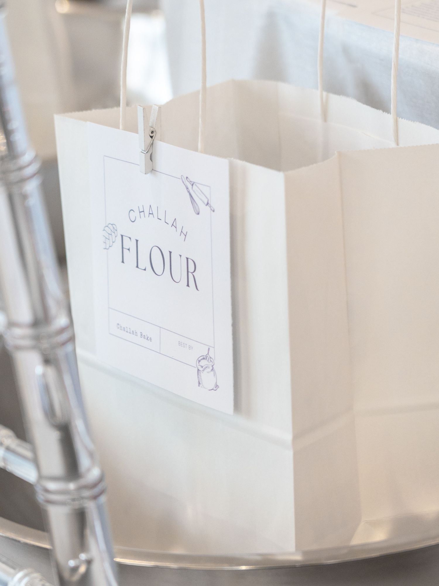 White paper gift bags with text labeled and arranged on silver chairs.