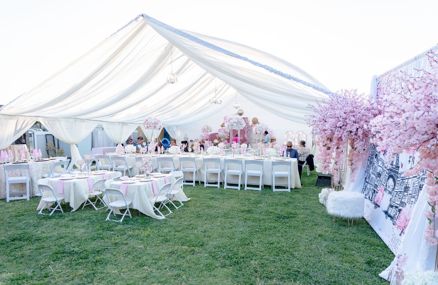 Large white wedding tent set up on grass with cherry blossom trees and guest seating.