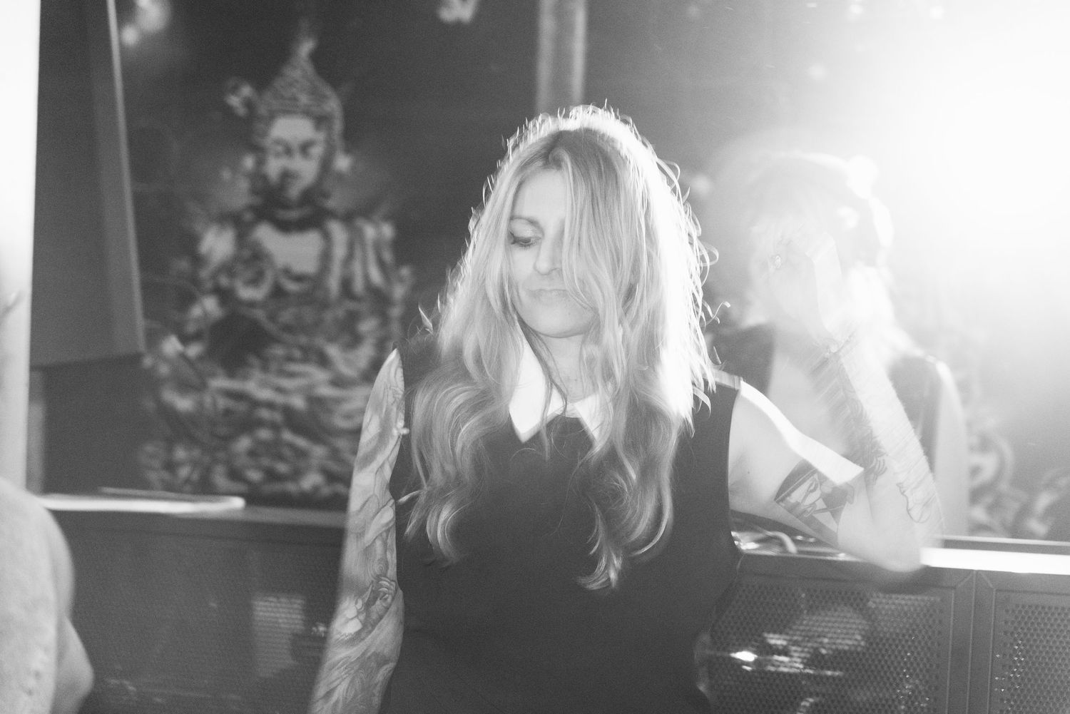 Black and white photo of a blonde woman reading a book with a Buddha statue in the background.