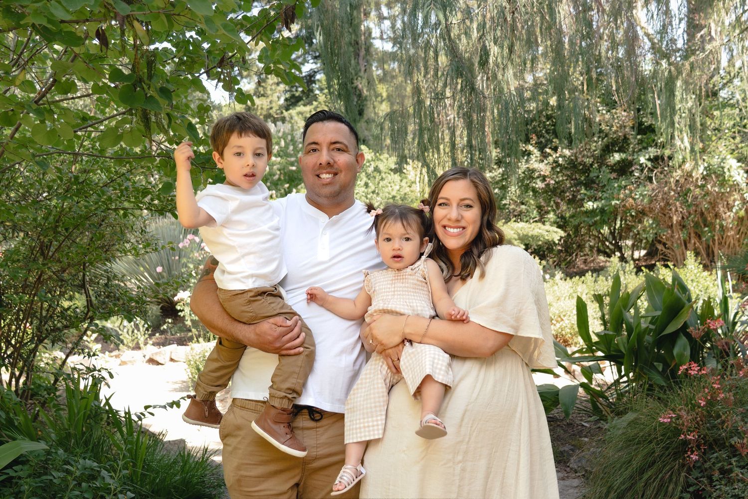 A happy family of four poses together in a lush garden setting.
