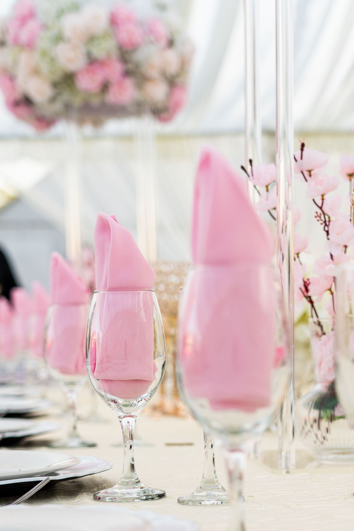 Pink napkins folded in wine glasses with cherry blossom branches for wedding table decor.