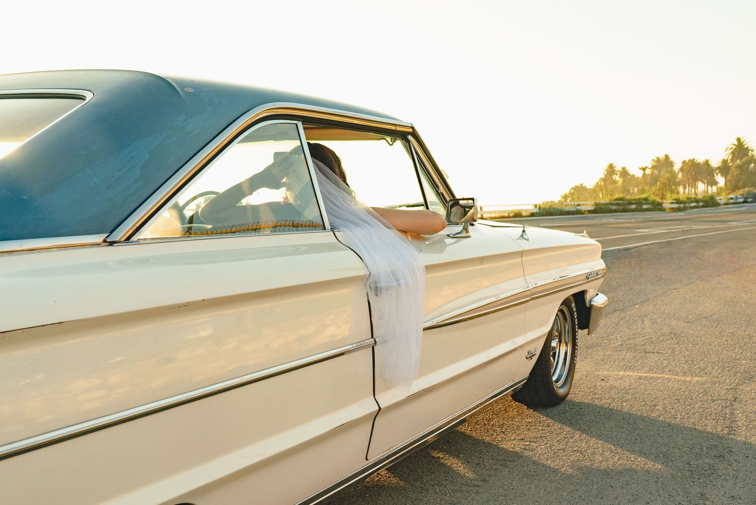 Vintage cream classic car with blue roof parked on pavement at golden hour sunset.
