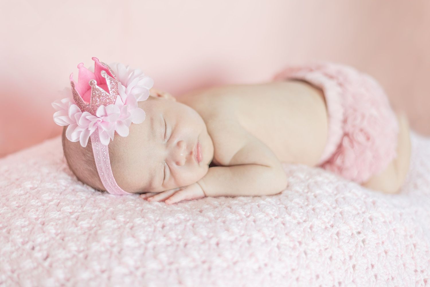 Delicate newborn photography with pink floral accessories on soft textured background.
