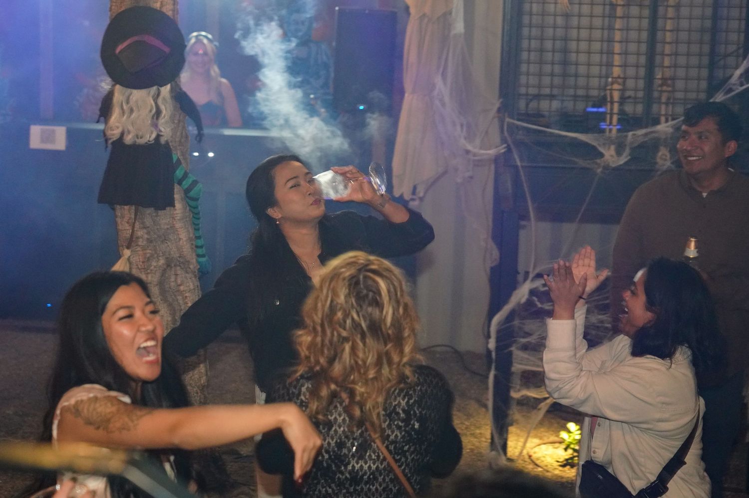 Group of young adults enjoying a Halloween party with decorations, smoke, and festive atmosphere indoors.