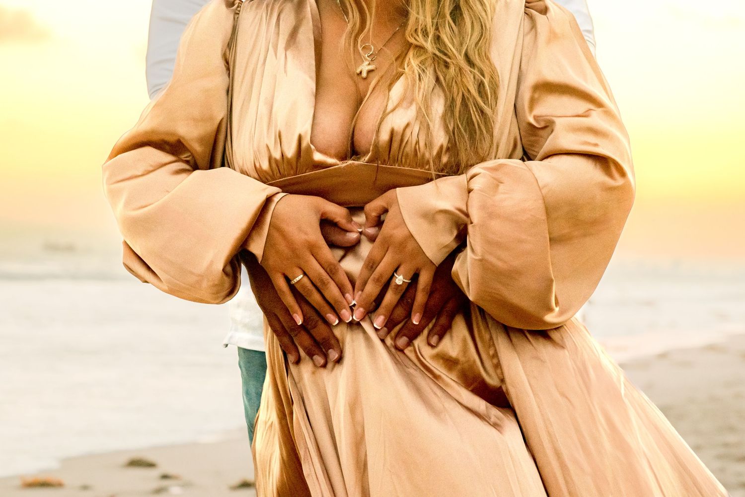 Close up of hands forming heart shape against flowing champagne dress.