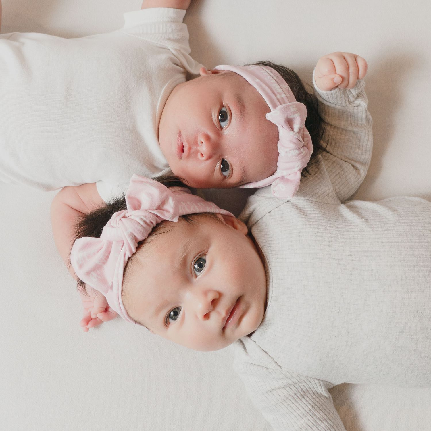 Baby wearing white onesie lying on textured fabric looking up at camera.