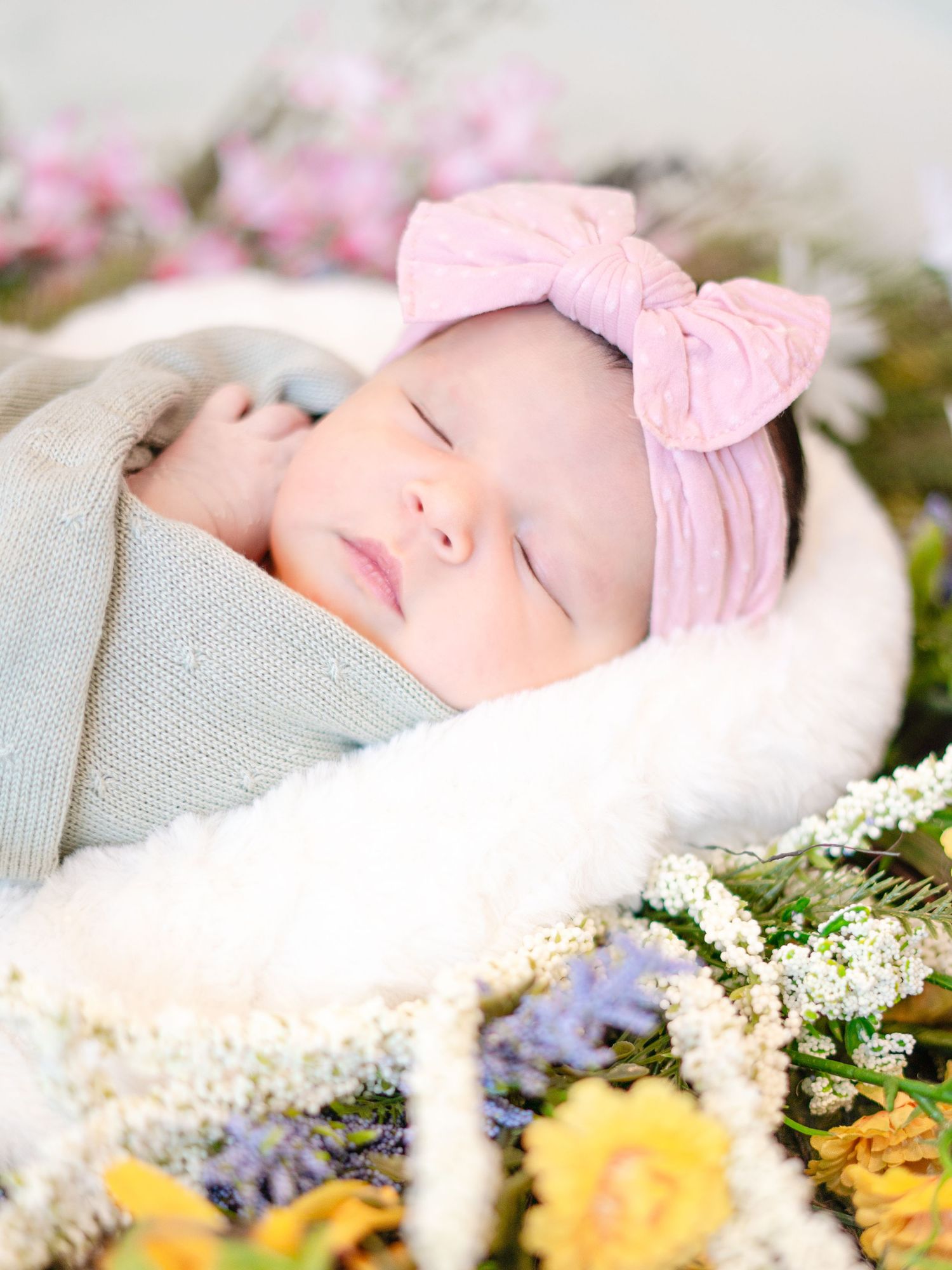 A baby lying on soft fabric surrounded by delicate flowers and greenery.