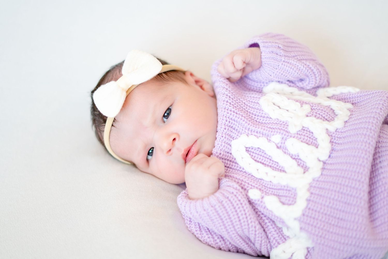 A baby wearing a purple knit outfit lying on a white surface.
