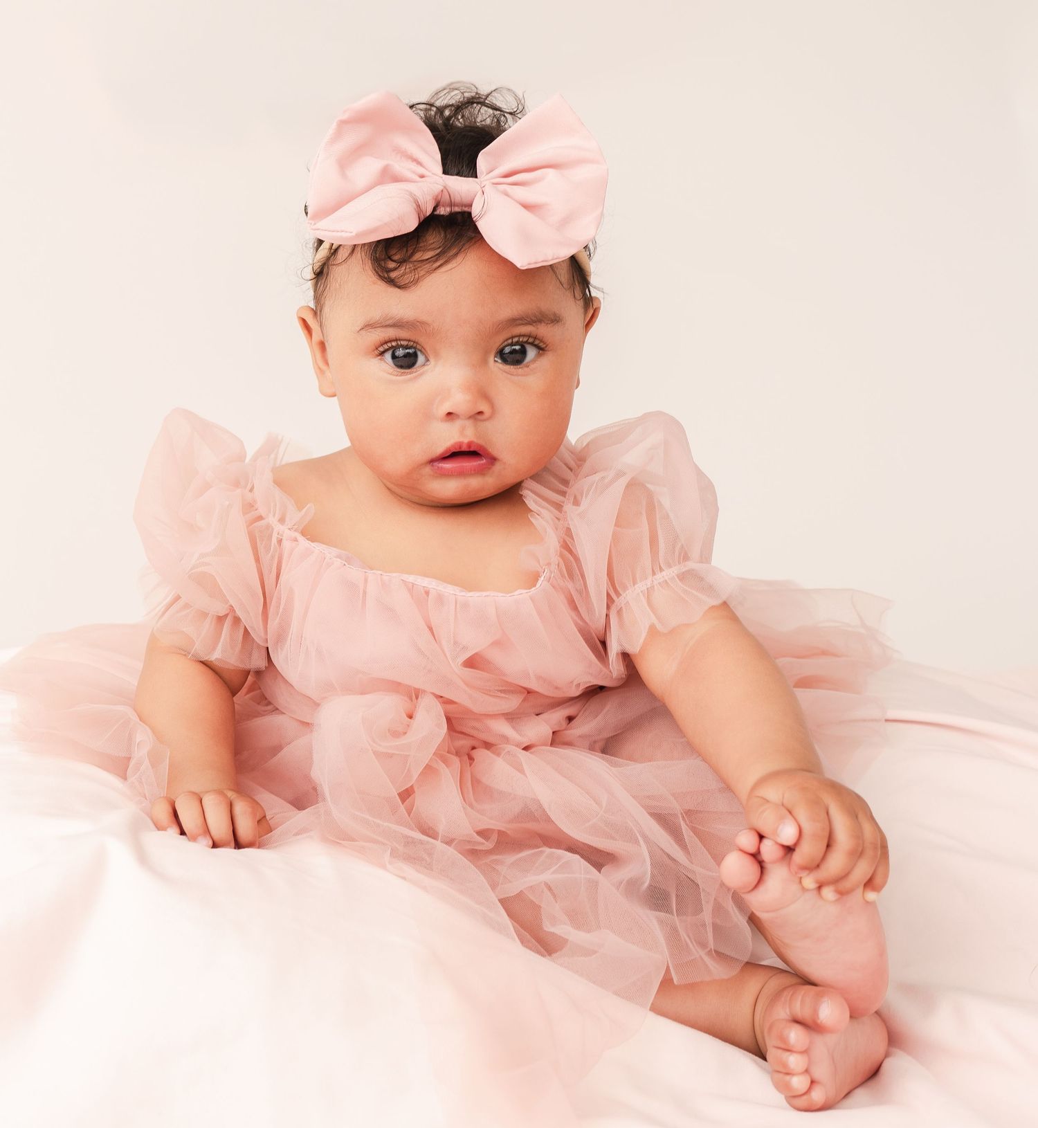 Baby in pink tulle dress laying on cream background during 6 month milestone photo session.