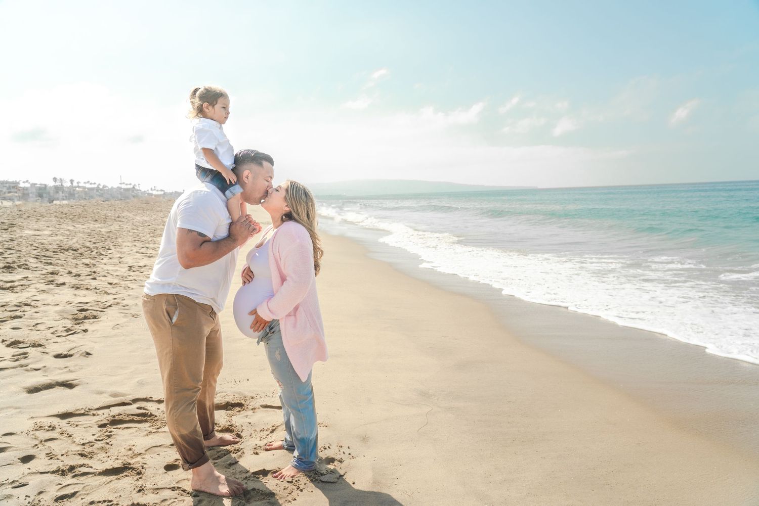 Intimate family photoshoot on a serene beach with gentle waves and sandy shoreline.