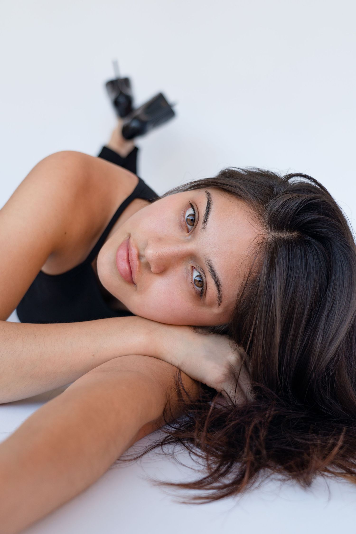 A portrait of a person with dark hair in black clothing laying against a white background.