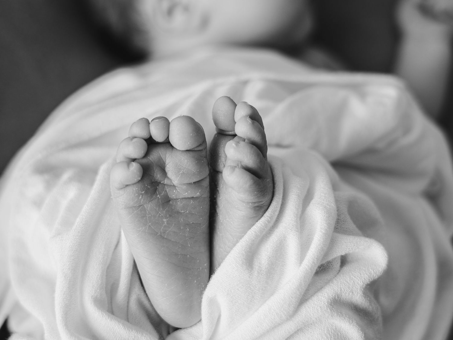 Black and white macro shot of baby's tiny toes and feet against white fabric.